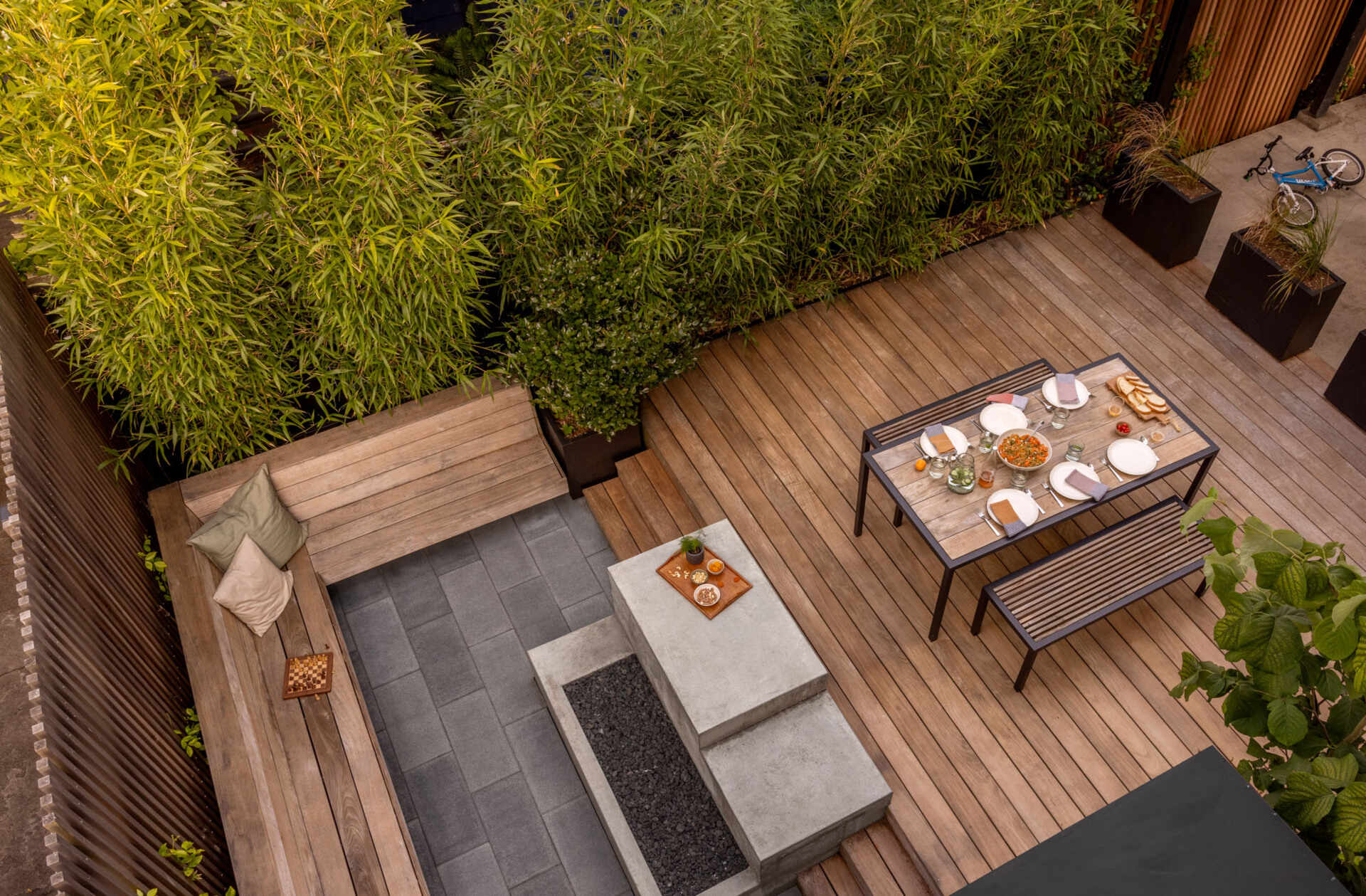 A compact backyard transforms into a layered outdoor retreat with a firepit, built-in seating, and a playful corner window connection.