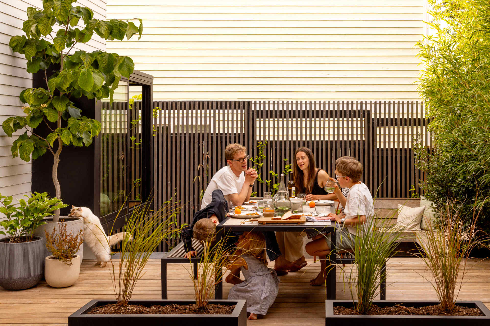 A compact backyard transforms into a layered outdoor retreat with a firepit, built-in seating, and a playful corner window connection.
