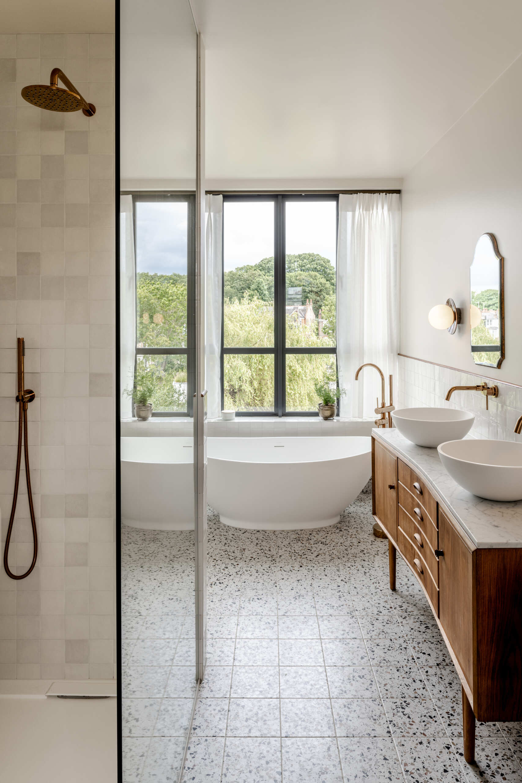 The bedroom and bathroom continue the restrained material palette, while slim steel-framed dormer windows carry the architectural language of the extension to the upper level.