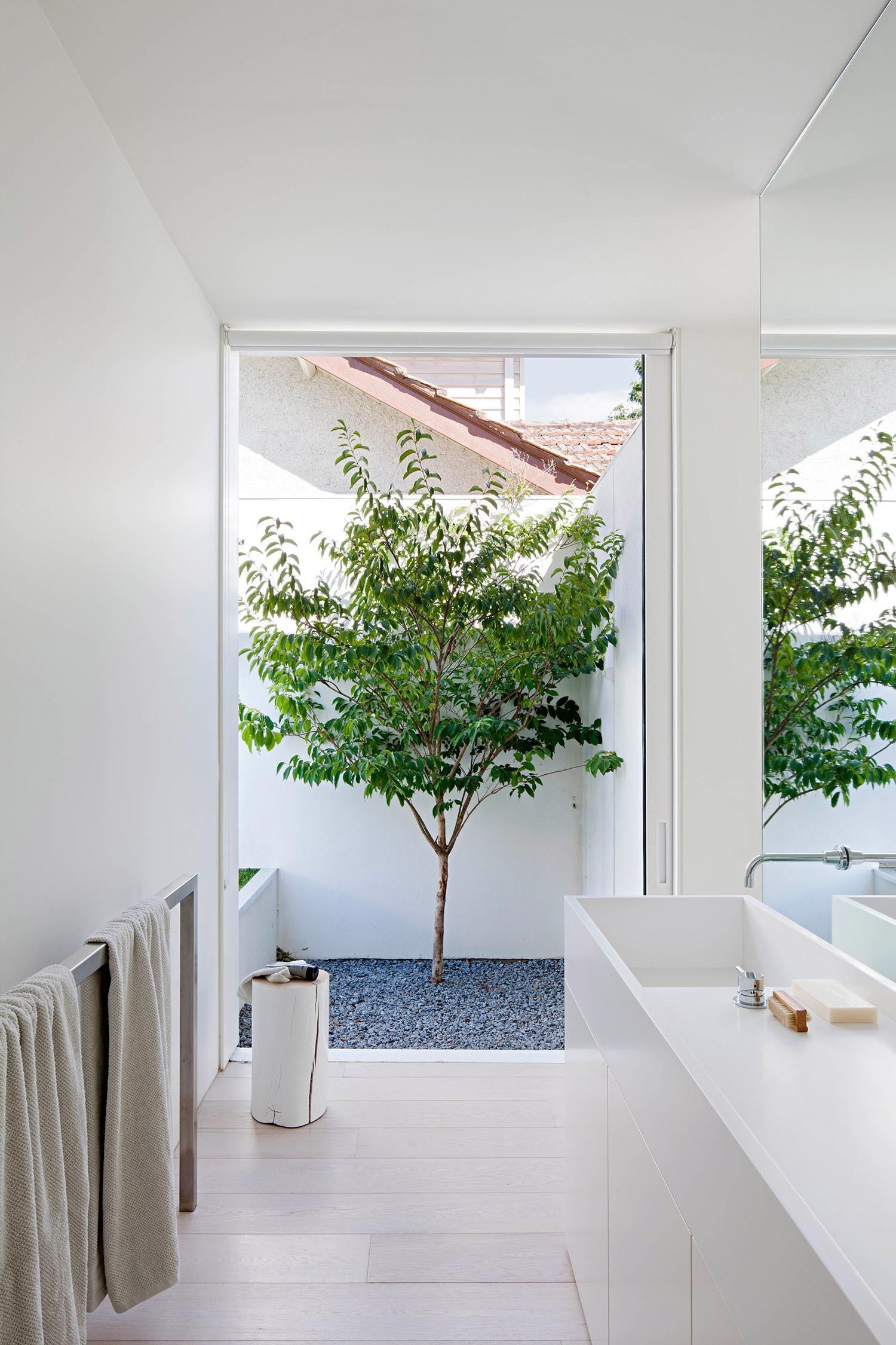 A large window, simple vanity, and freestanding towel bar create a serene, light filled bathroom that reflects the home’s restrained aesthetic.