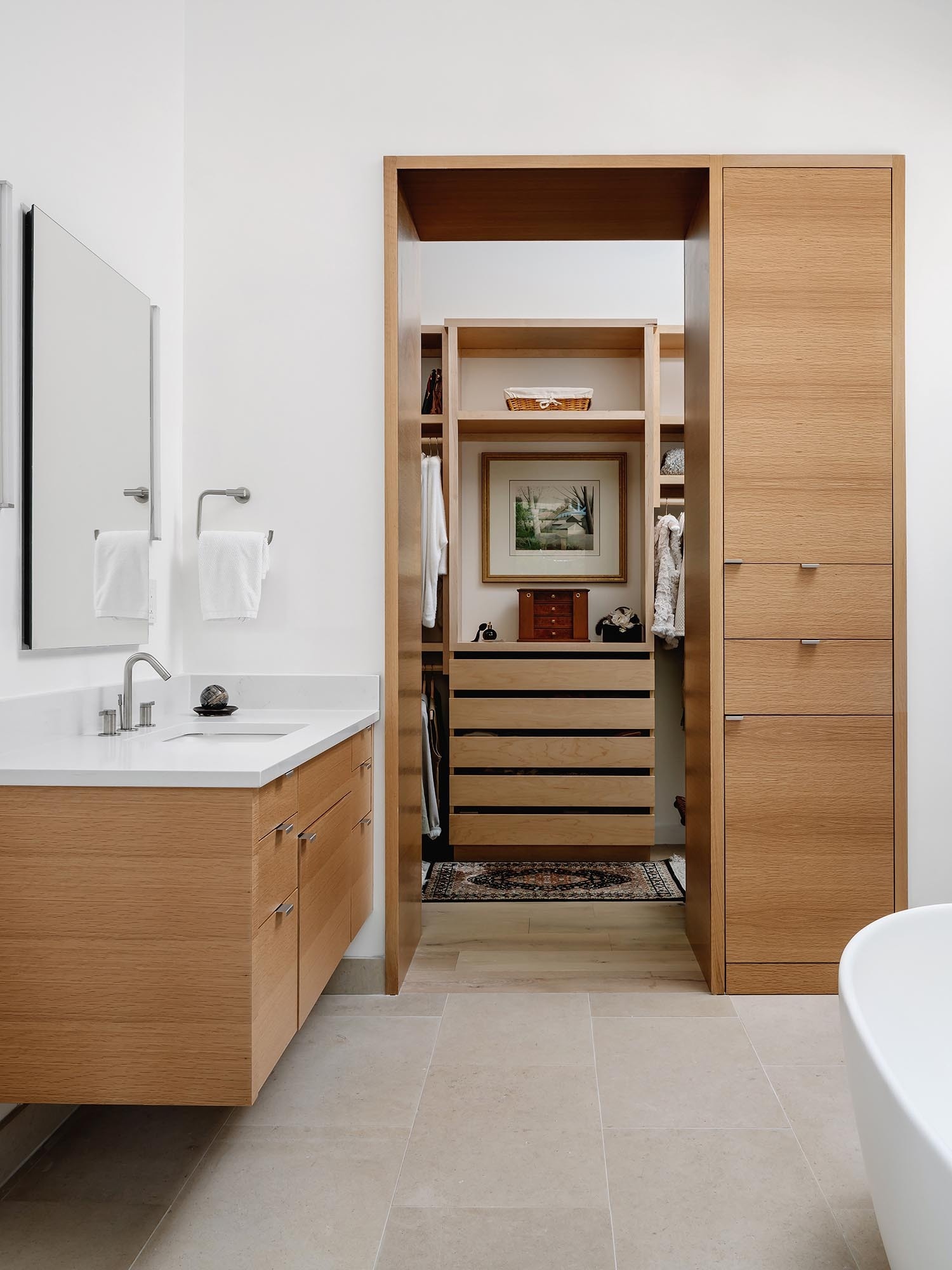 Limestone floors and walls surround a freestanding bathtub and elegant chandelier in this Austin bathroom, creating a calm spa like atmosphere connected to a walk in closet.