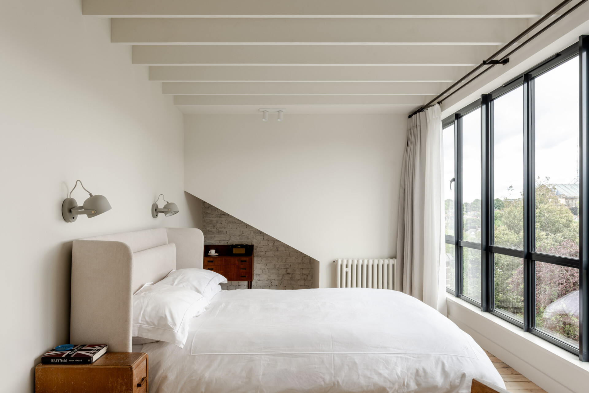 The bedroom and bathroom continue the restrained material palette, while slim steel-framed dormer windows carry the architectural language of the extension to the upper level.