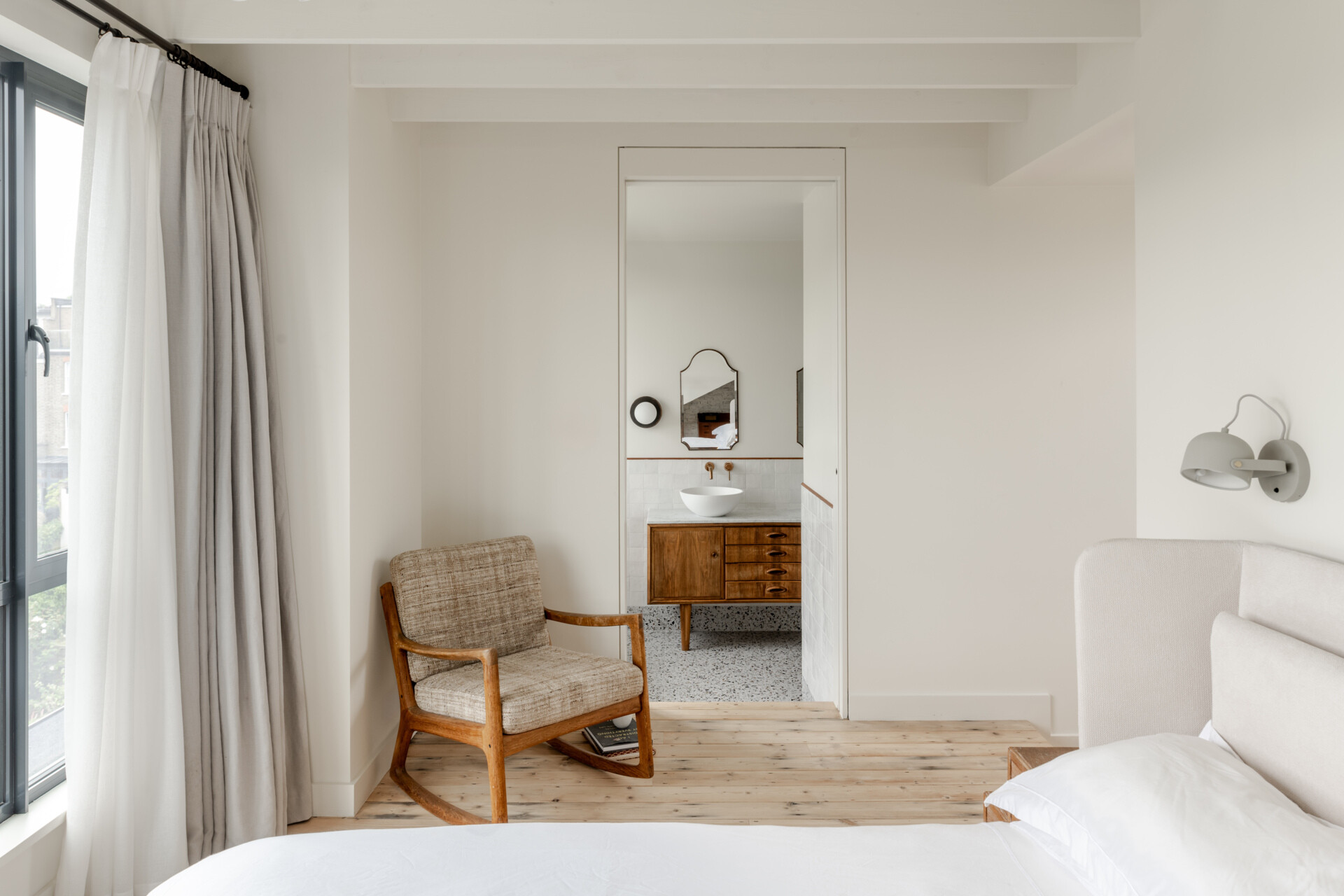 The bedroom and bathroom continue the restrained material palette, while slim steel-framed dormer windows carry the architectural language of the extension to the upper level.