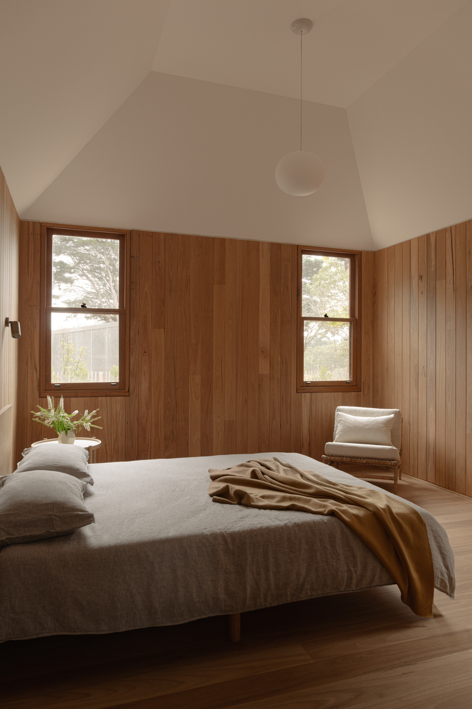 In the bedroom pavilion, tongue-and-groove timber linings and steep raked ceilings create a quieter spatial character within the private wing of the house.