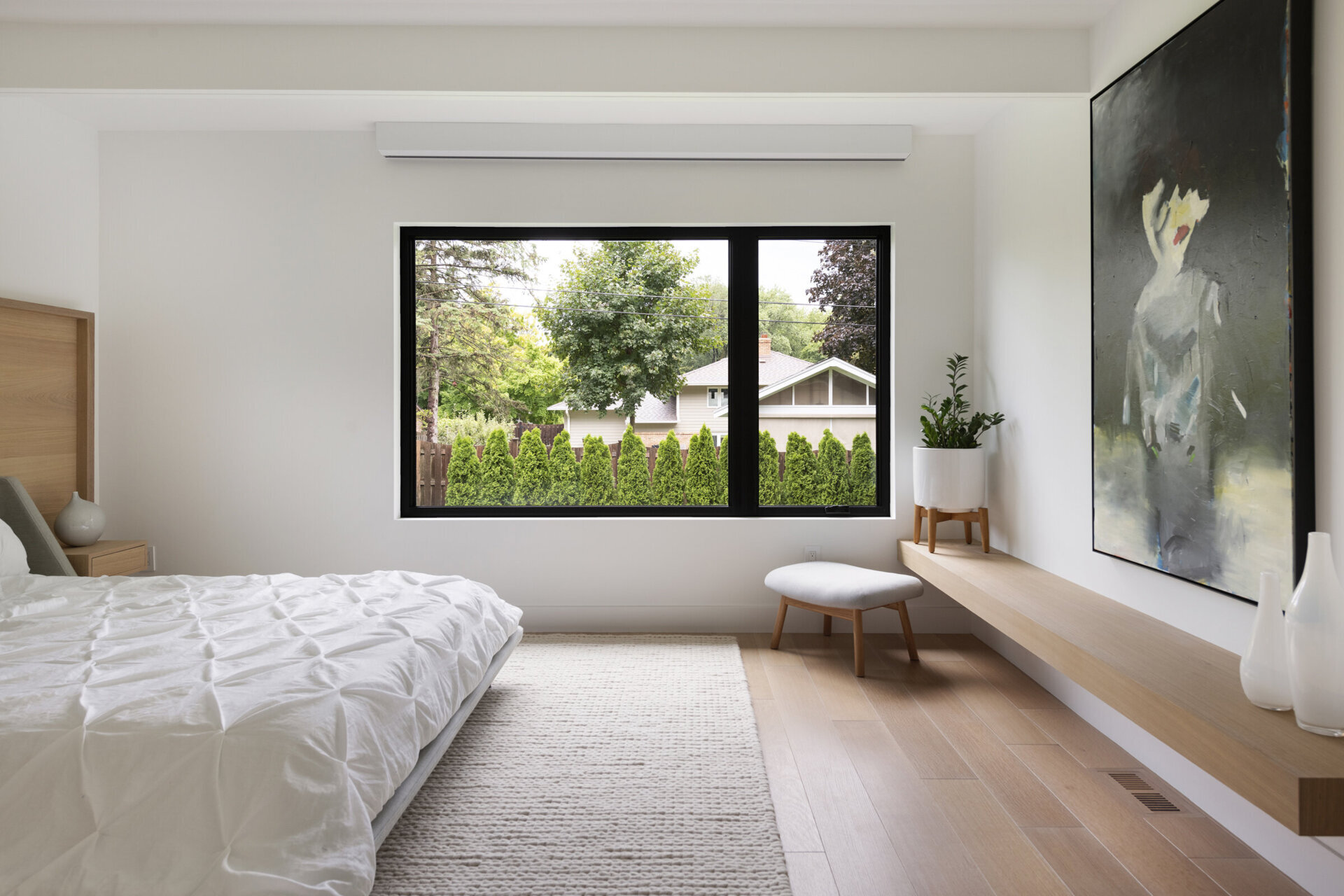 Los dormitorios están escondidos detrás de puertas ocultas entre la cocina y el comedor, mostrando un diseño bien pensado. Una cabecera de madera con una mesa auxiliar incorporada aporta un elemento natural al interior, complementando los estantes flotantes de madera en toda la habitación.