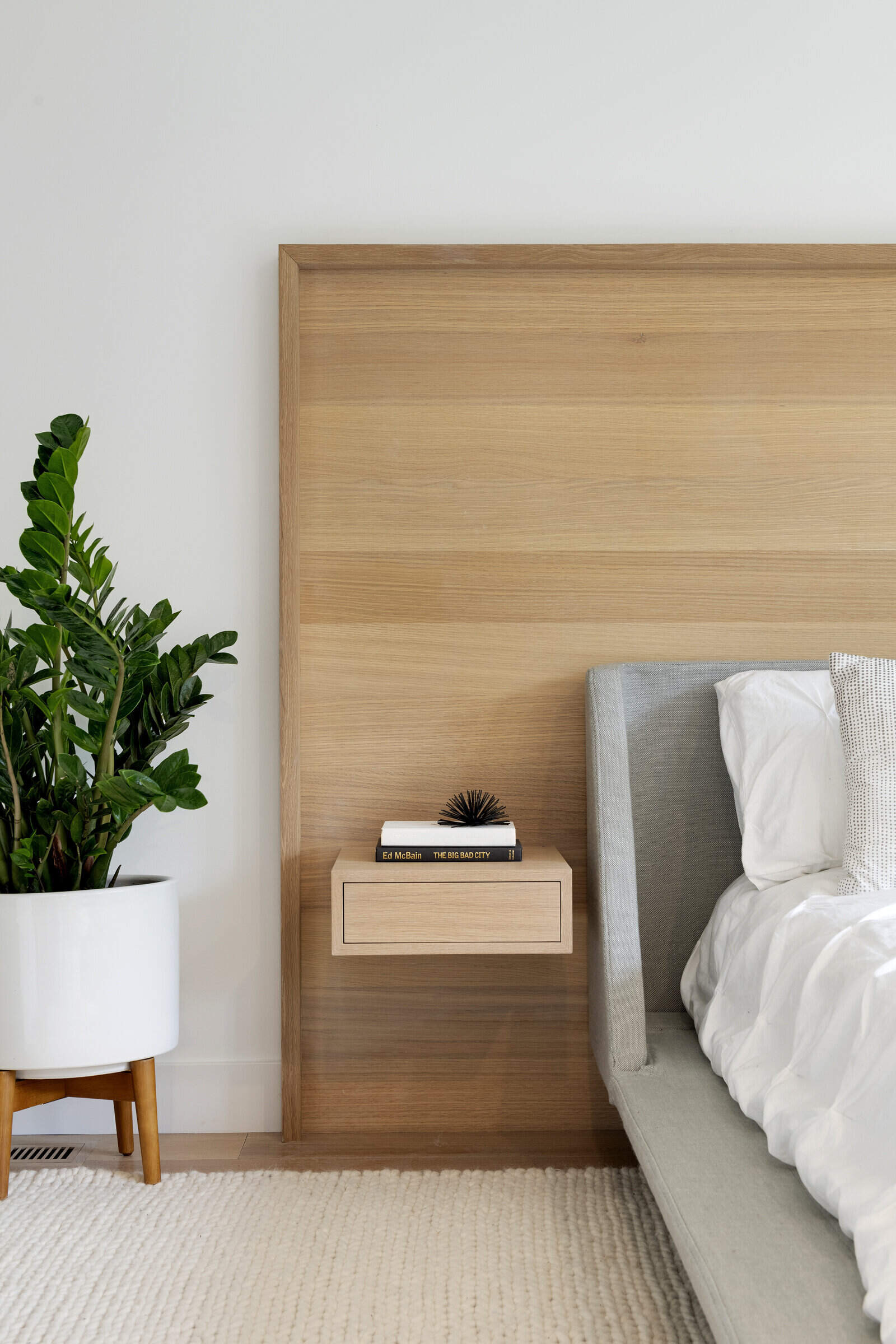 Los dormitorios están escondidos detrás de puertas ocultas entre la cocina y el comedor, mostrando un diseño bien pensado. Una cabecera de madera con una mesa auxiliar incorporada aporta un elemento natural al interior, complementando los estantes flotantes de madera en toda la habitación.