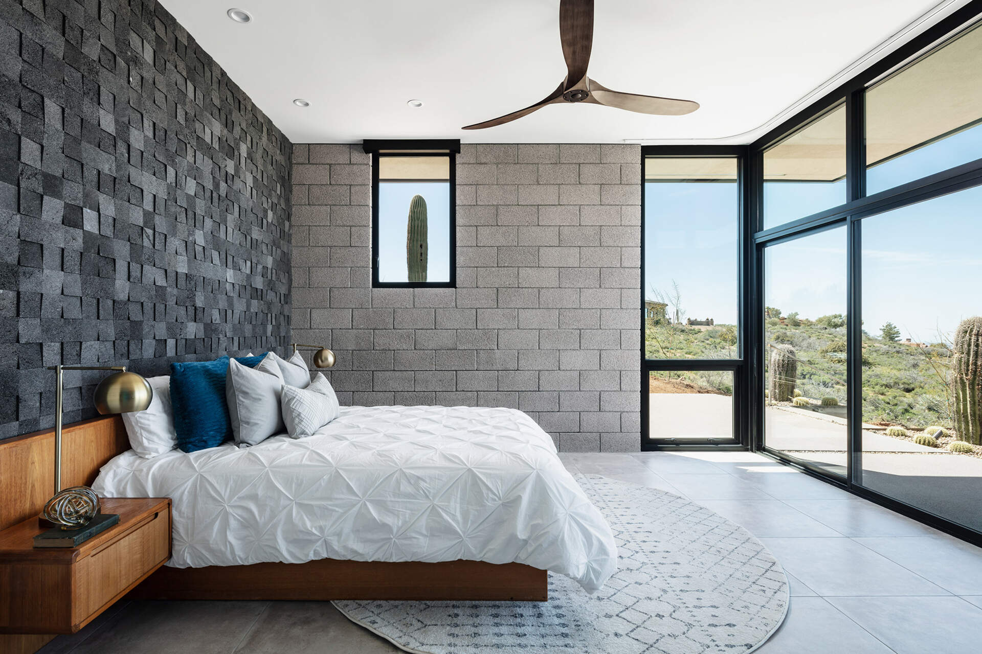 A minimalist bedroom with desert views and a textured lava rock feature wall.