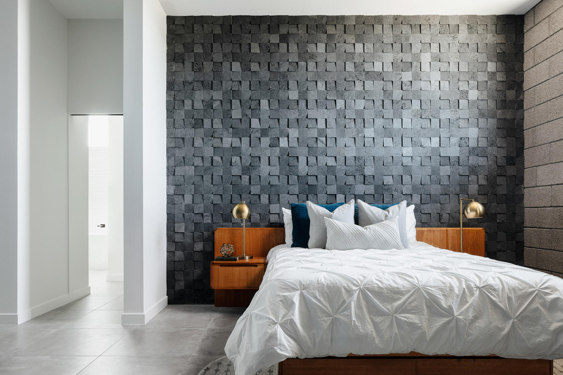 A minimalist bedroom with desert views and a textured lava rock feature wall.