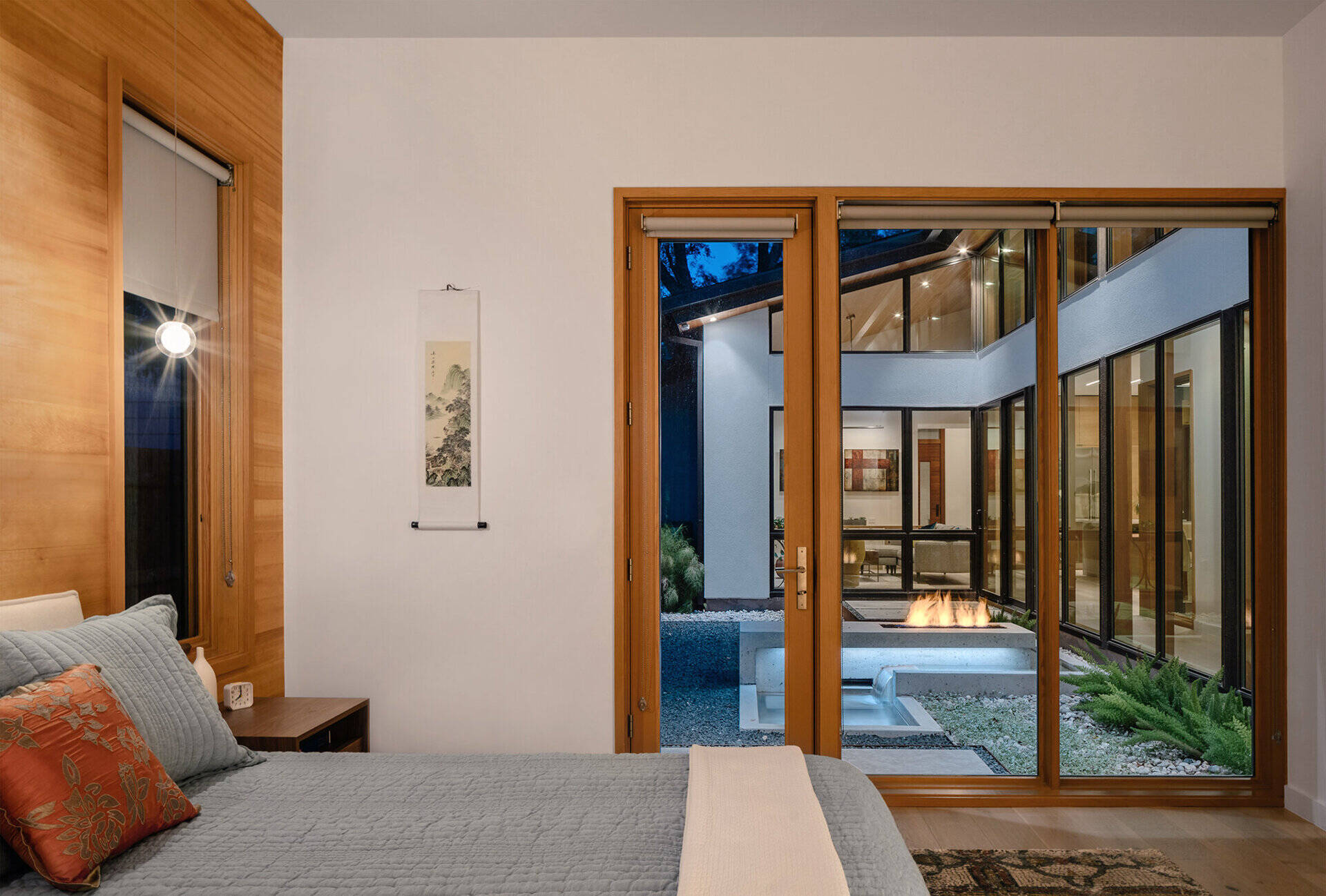 A warm wood accent wall and a door leading outdoors give this Austin bedroom a calm, grounded atmosphere that connects the private interior space with nature.