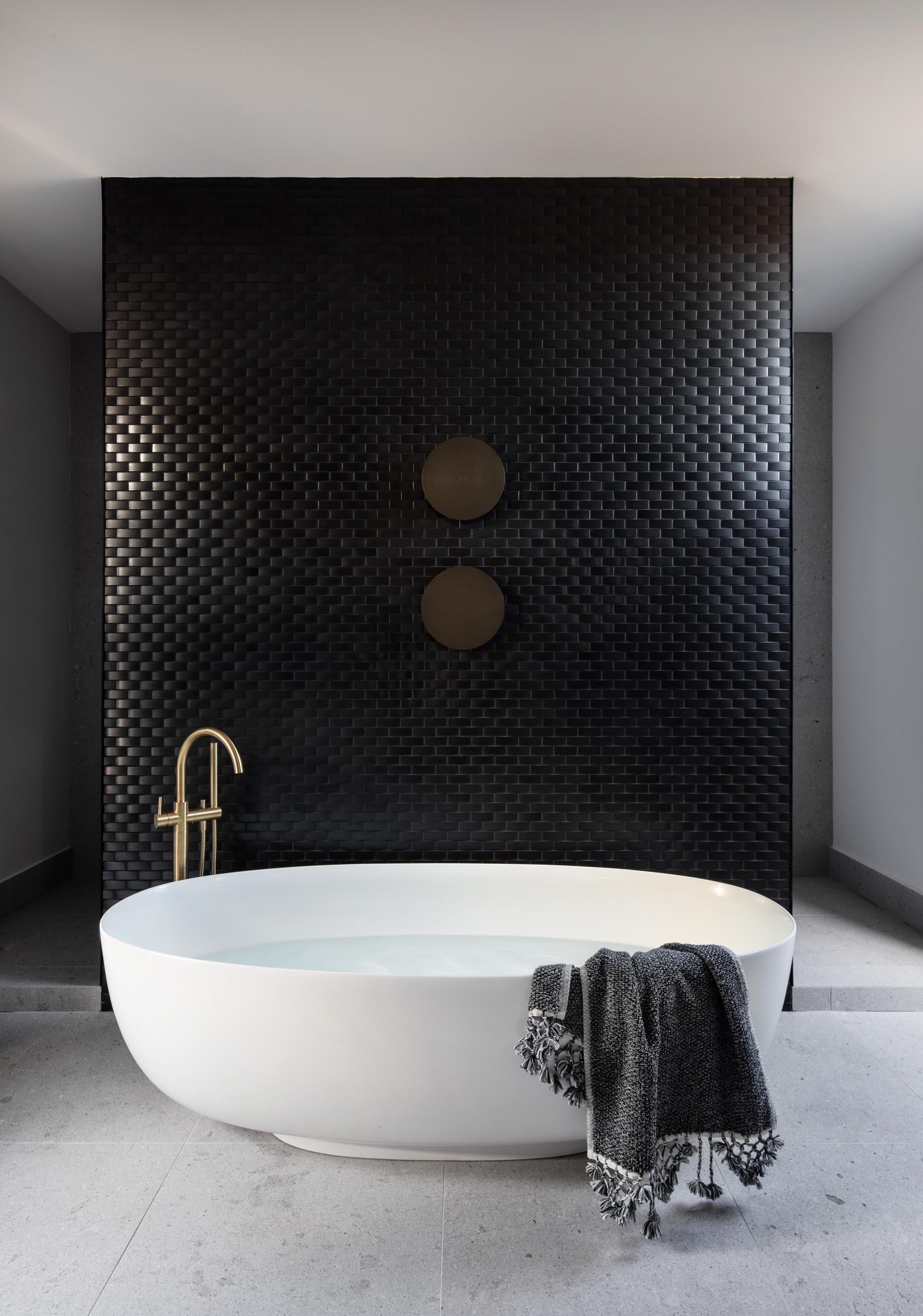 Black tiled walls, round mirrors, and a freestanding oval bathtub define the master bathroom, which connects to a walk-in closet with dark wood cabinetry.