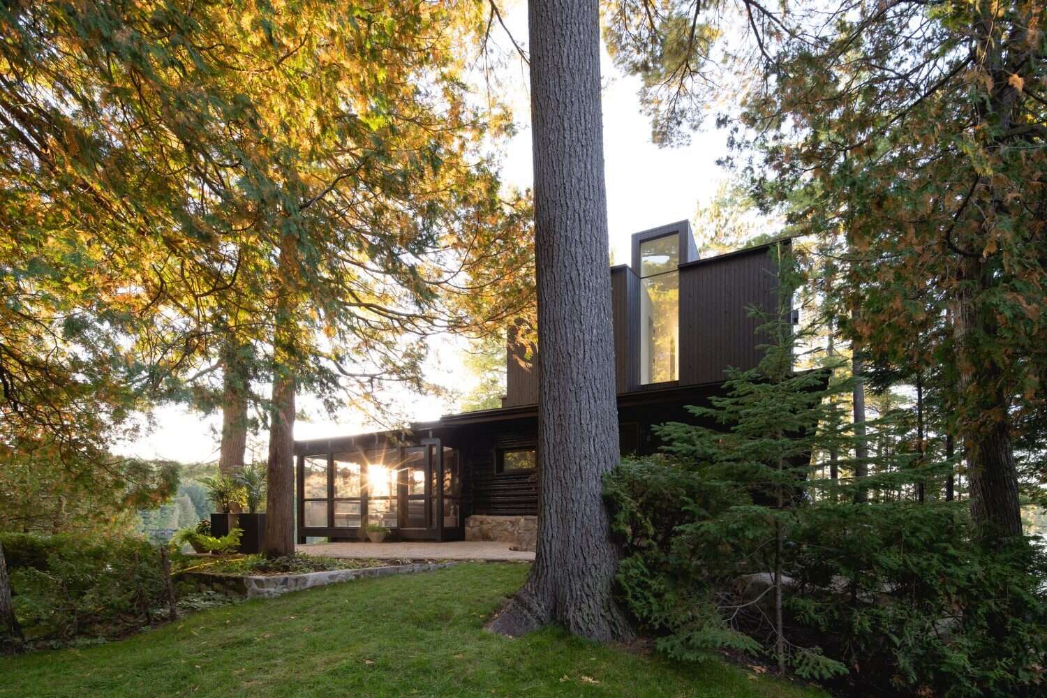 A log cabin on a rocky point in Quebec was given a contemporary second life by Paul Bernier Architecte. The remodel adds a second level and a screened porch while preserving the rustic character of the original chalet. A dark exterior and stone foundation help the cabin blend into the surrounding landscape and lakeshore.