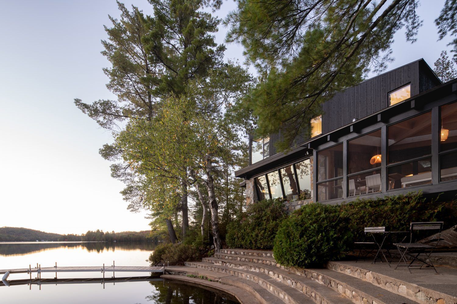 A log cabin on a rocky point in Quebec was given a contemporary second life by Paul Bernier Architecte. The remodel adds a second level and a screened porch while preserving the rustic character of the original chalet. A dark exterior and stone foundation help the cabin blend into the surrounding landscape and lakeshore.