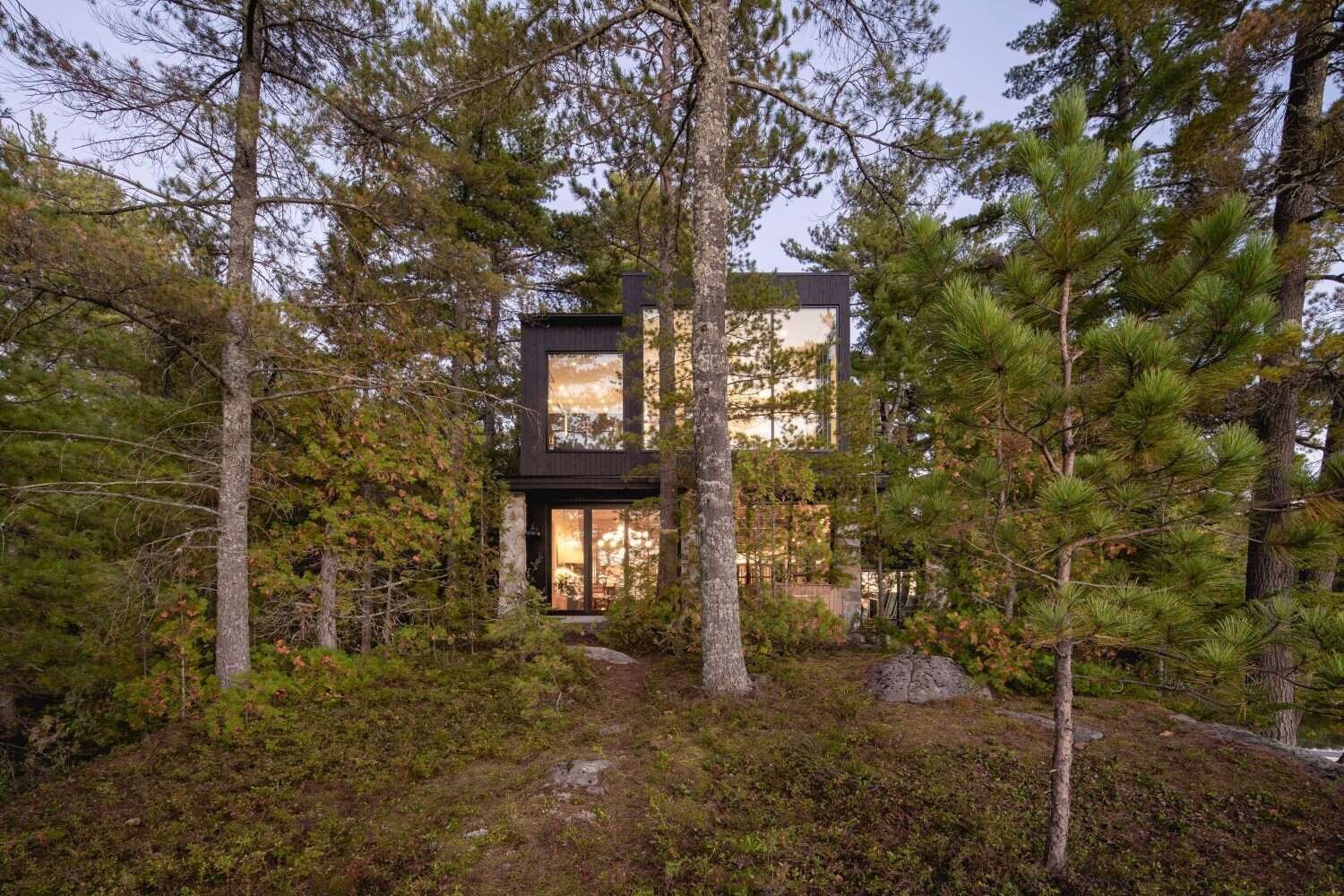 A log cabin on a rocky point in Quebec was given a contemporary second life by Paul Bernier Architecte. The remodel adds a second level and a screened porch while preserving the rustic character of the original chalet. A dark exterior and stone foundation help the cabin blend into the surrounding landscape and lakeshore.