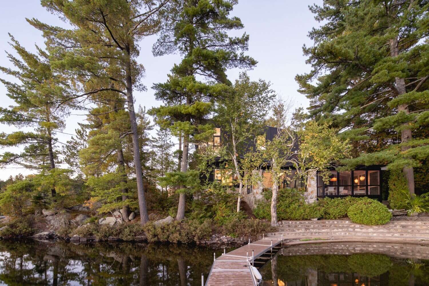 A log cabin on a rocky point in Quebec was given a contemporary second life by Paul Bernier Architecte. The remodel adds a second level and a screened porch while preserving the rustic character of the original chalet. A dark exterior and stone foundation help the cabin blend into the surrounding landscape and lakeshore.