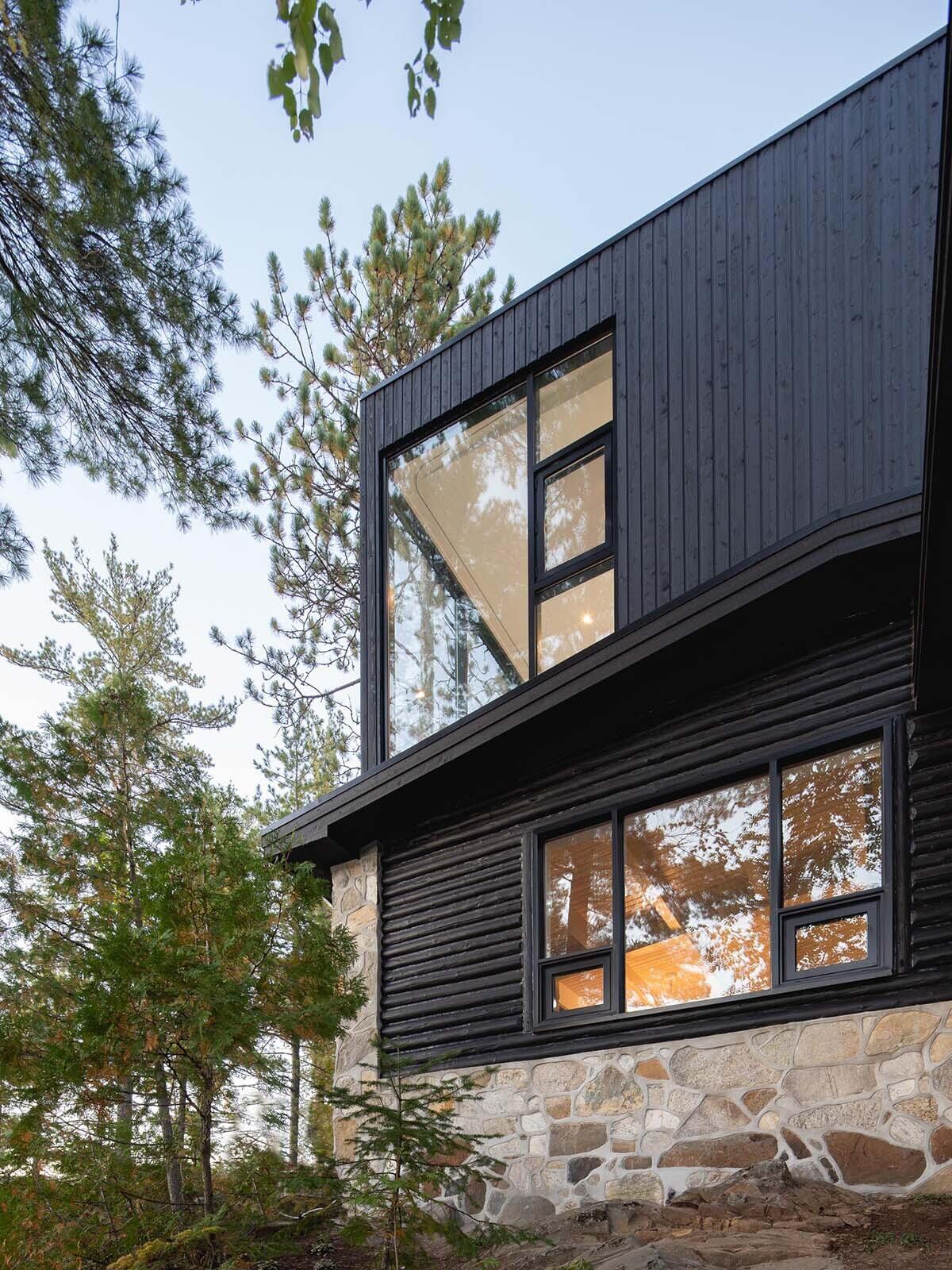 A log cabin on a rocky point in Quebec was given a contemporary second life by Paul Bernier Architecte. The remodel adds a second level and a screened porch while preserving the rustic character of the original chalet. A dark exterior and stone foundation help the cabin blend into the surrounding landscape and lakeshore.