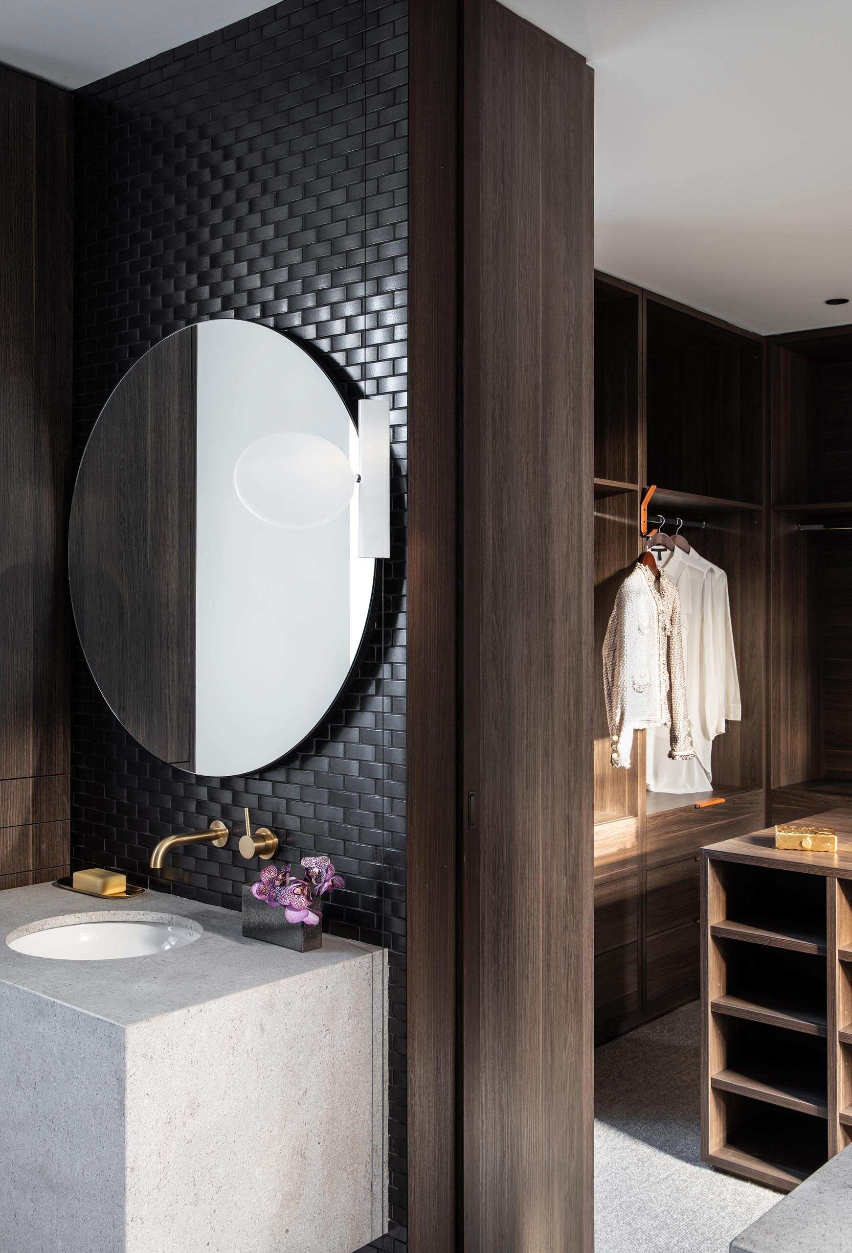 Black tiled walls, round mirrors, and a freestanding oval bathtub define the master bathroom, which connects to a walk-in closet with dark wood cabinetry.