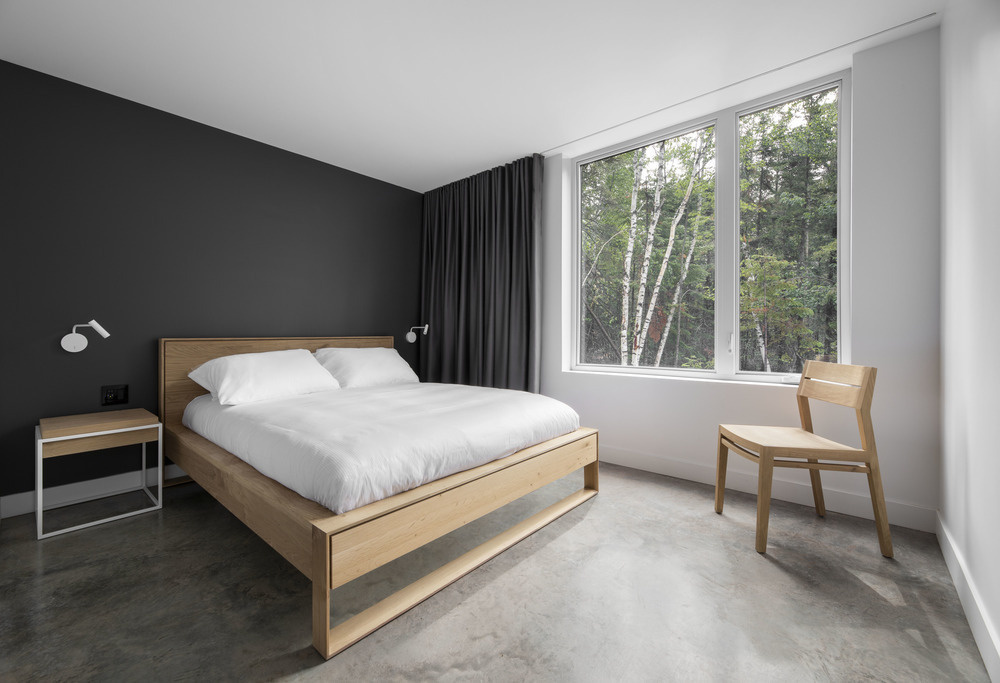 A separate bedroom features a matte black accent wall, black curtains, and an en-suite bathroom with large black tiles and a wood vanity that echoes the bedroom’s warmth and texture.