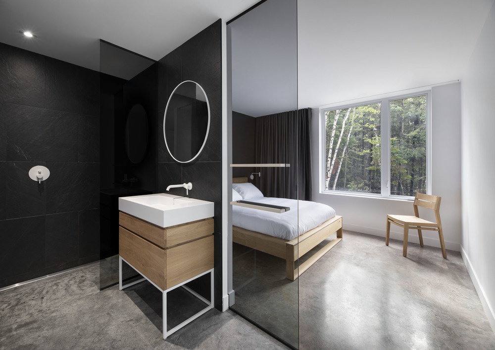 A separate bedroom features a matte black accent wall, black curtains, and an en-suite bathroom with large black tiles and a wood vanity that echoes the bedroom’s warmth and texture.