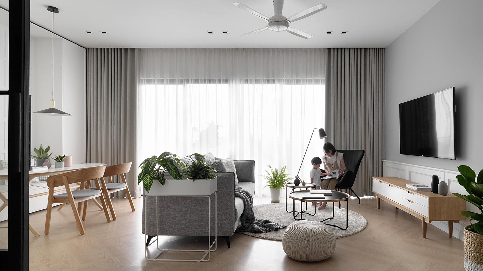 The living room in this apartment pairs a gray accent wall and sofa with light wood finishes and floor-to-ceiling curtains, creating a Scandinavian-inspired space that feels bright and relaxed.
