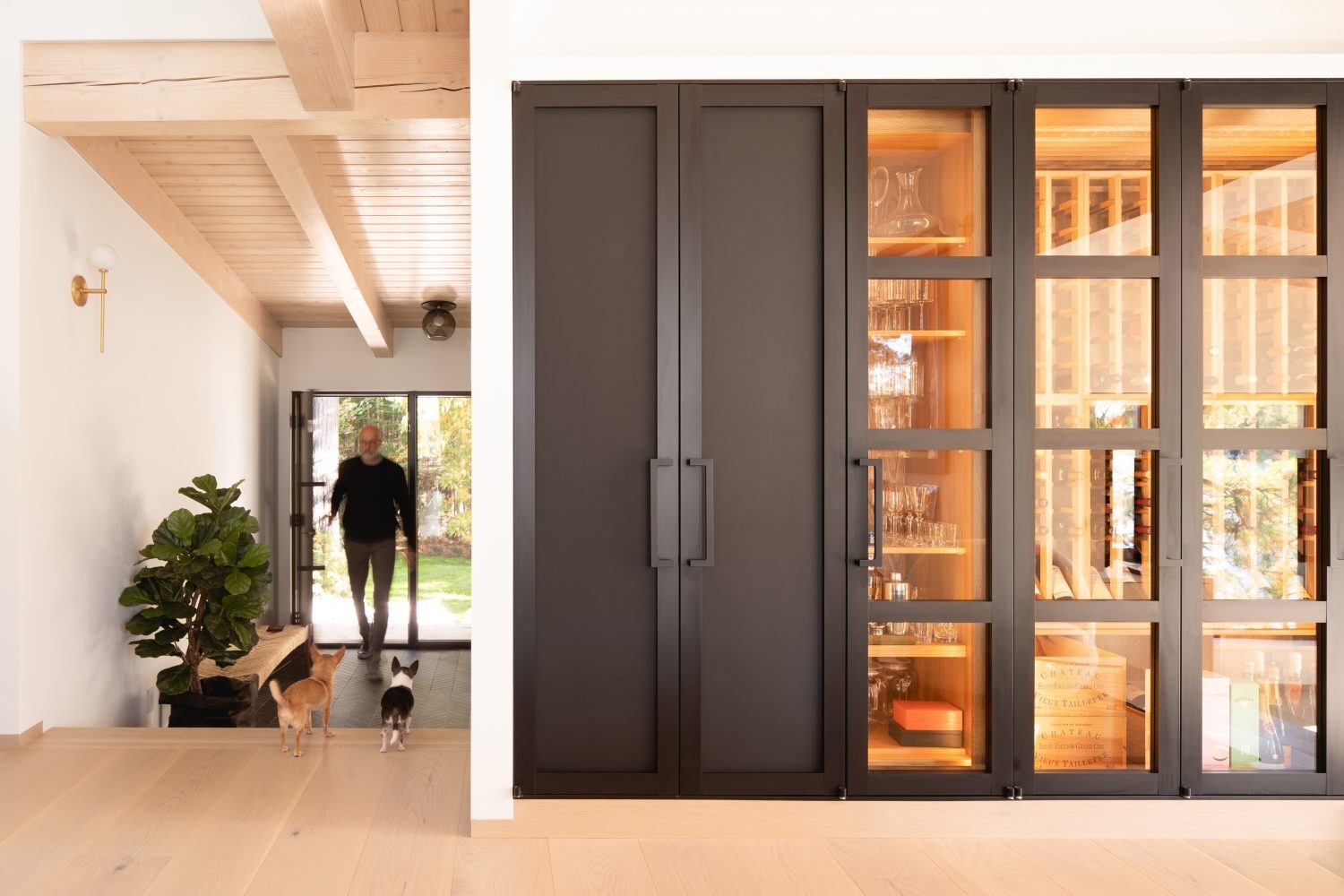 Steps from the entry lead into the social areas of the cabin, where a glass wine wall, black door accents, and angled windows add modern design moments within the rustic log interior.