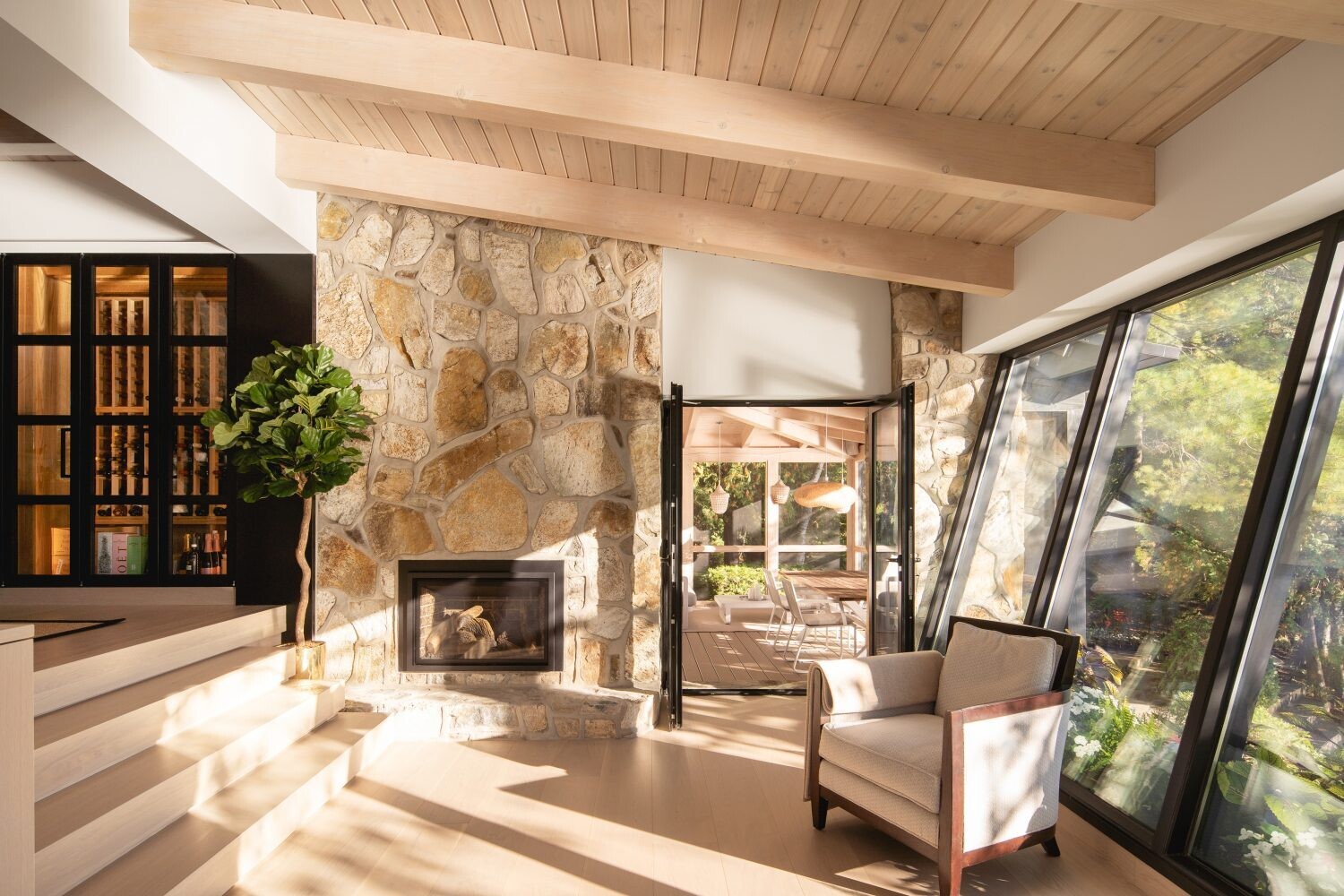 Steps from the entry lead into the social areas of the cabin, where a glass wine wall, black door accents, and angled windows add modern design moments within the rustic log interior.