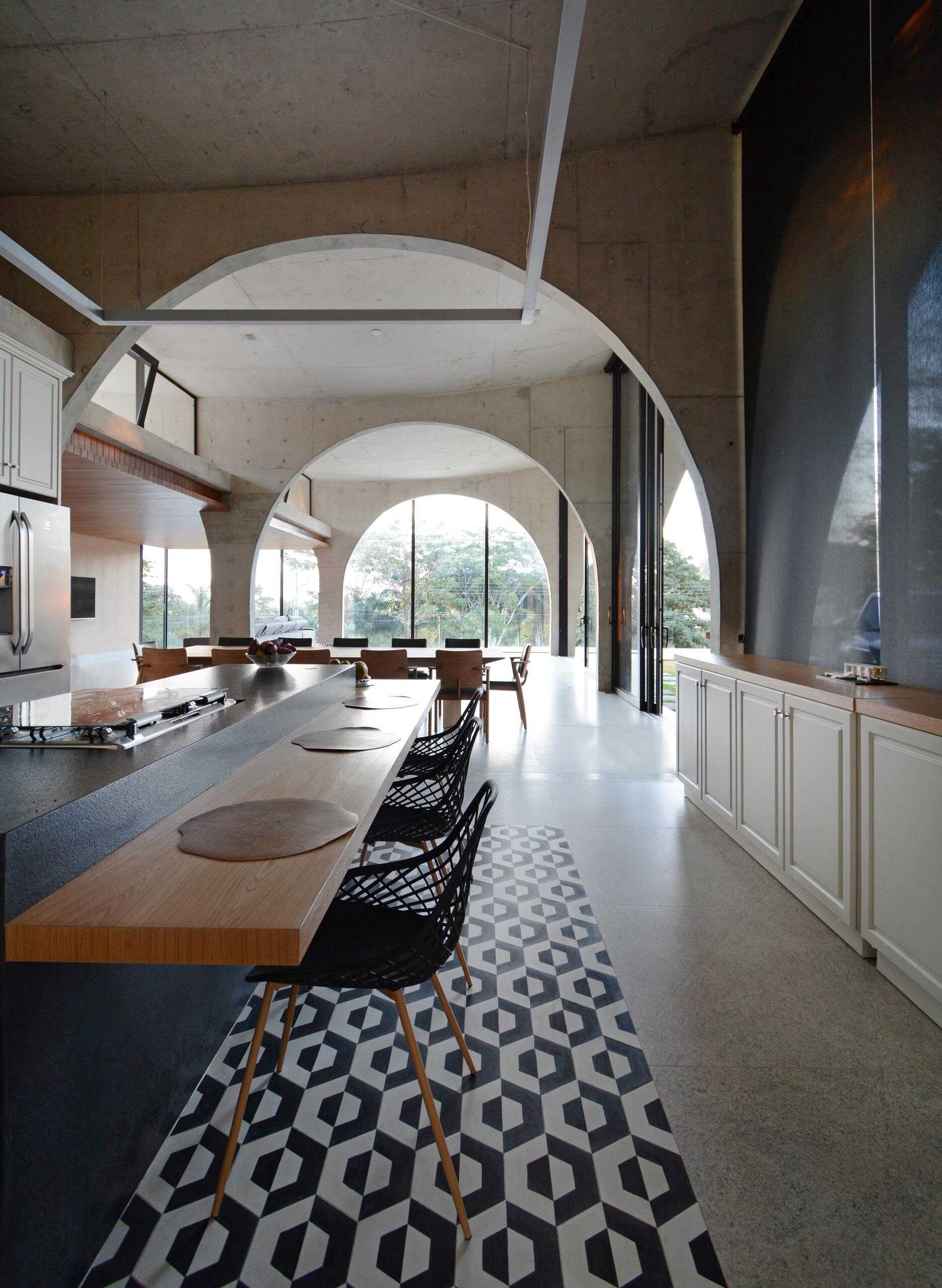 A long kitchen island anchors the social heart of the home while black framed windows follow the curves of the concrete arches above.