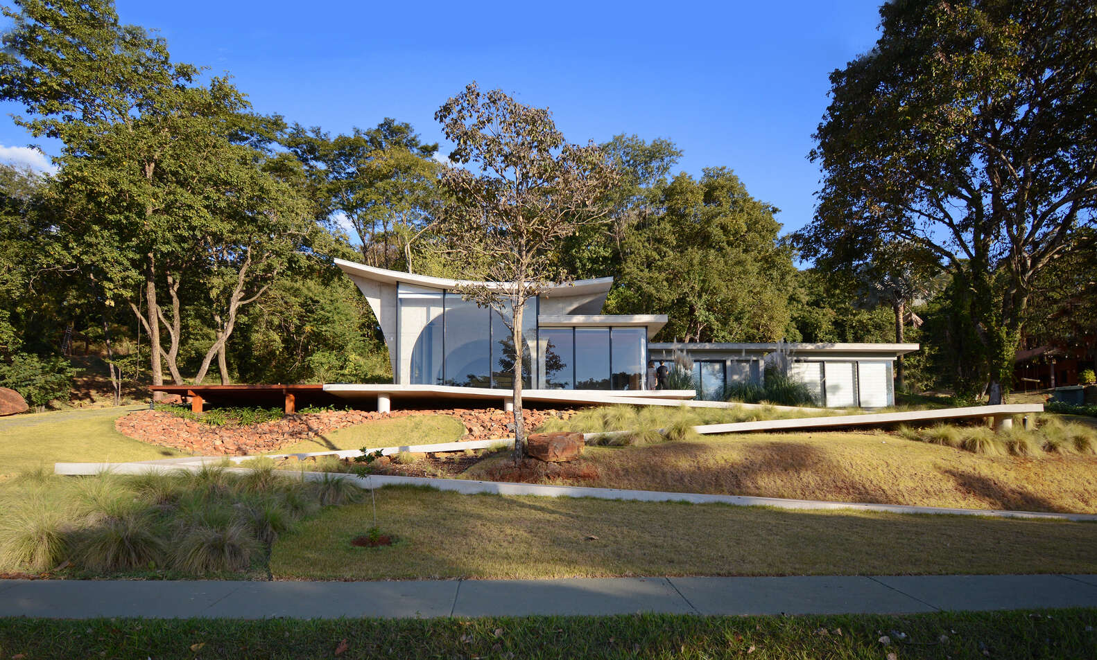 A winding concrete ramp leads up to Casa Joy in Brazil, revealing a sculptural modern home defined by six dramatic concrete arches and a concave roof overlooking the valley.