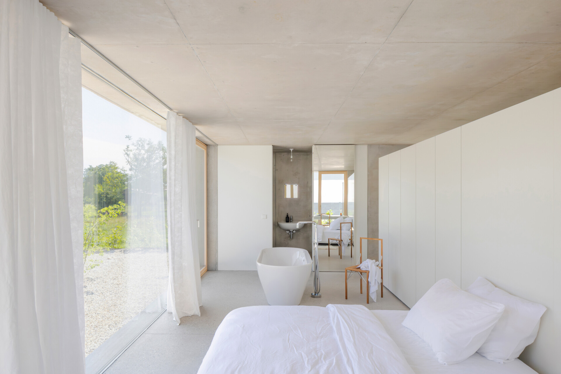 Sleeping and working spaces face a more intimate north east garden. The orientation creates a quieter atmosphere without breaking the openness of the plan. The bathroom is integrated within one of the concrete cores, with mirrored surfaces making the room feel larger.