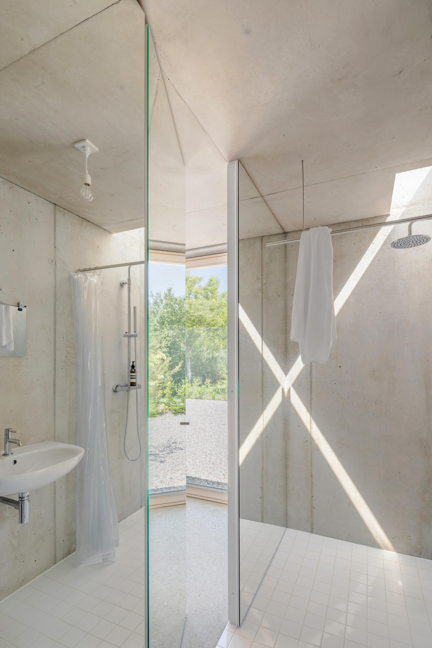 Sleeping and working spaces face a more intimate north east garden. The orientation creates a quieter atmosphere without breaking the openness of the plan. The bathroom is integrated within one of the concrete cores, with mirrored surfaces making the room feel larger.
