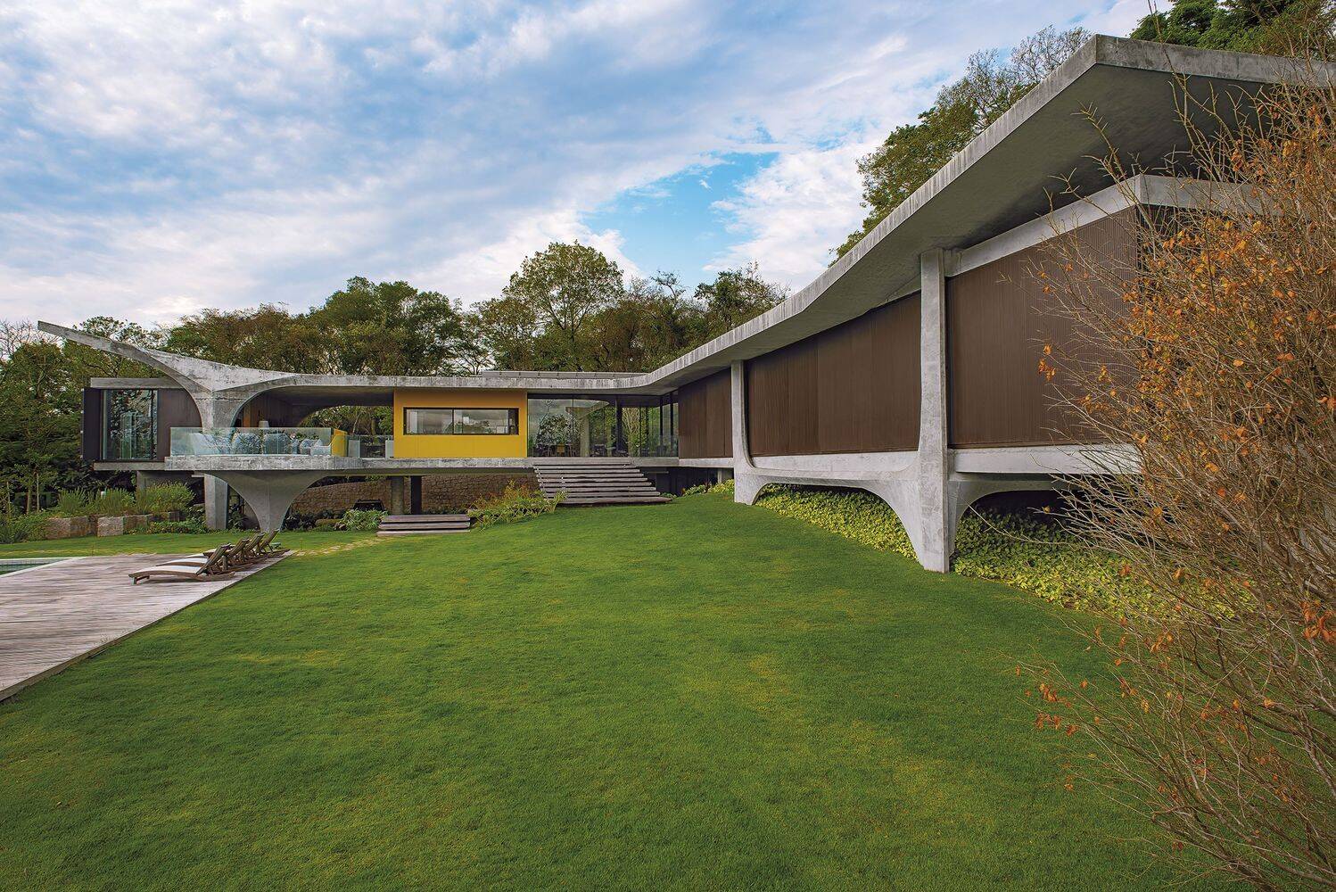 A modern concrete home designed to appear as if it floats above a sloped, tree-filled site, with sculptural pillars defining its bold architectural form.