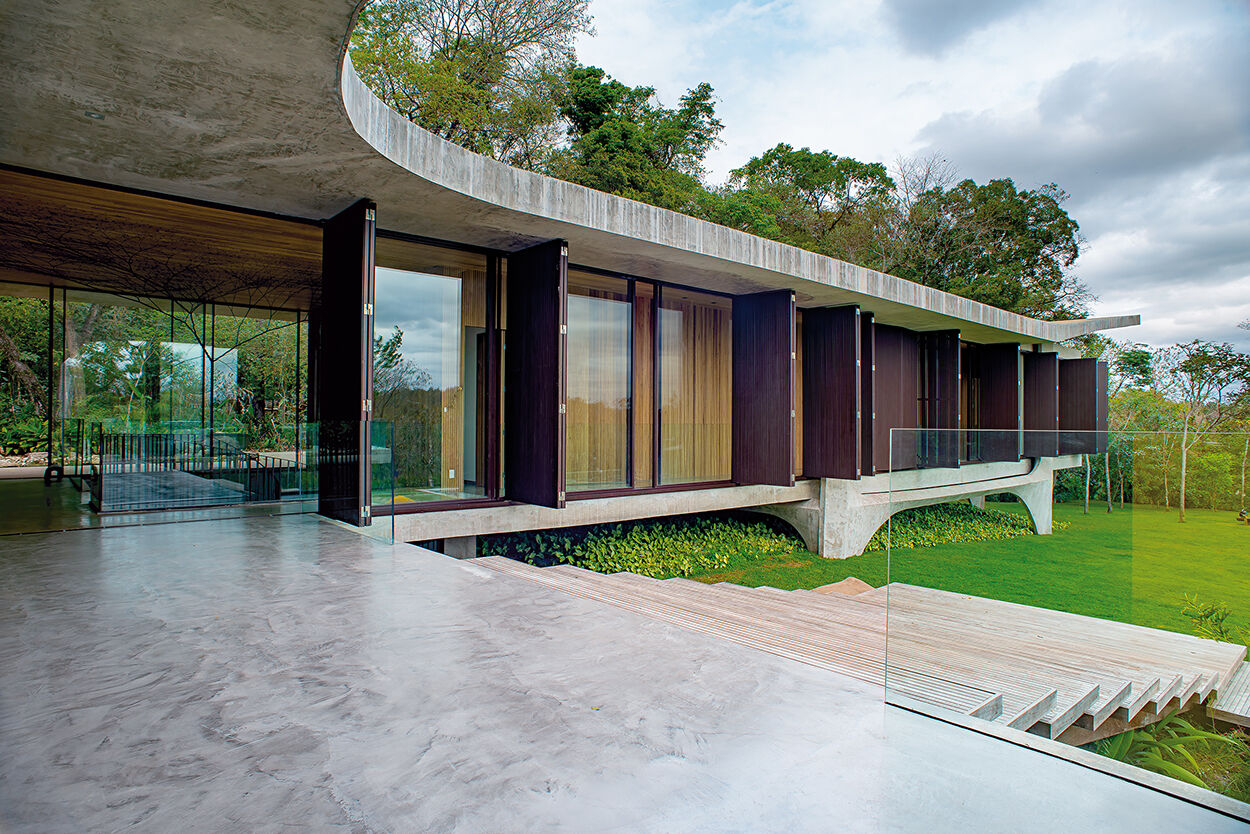 An expansive concrete balcony with wood stairs leading to outdoor spaces, extending the home across multiple levels.