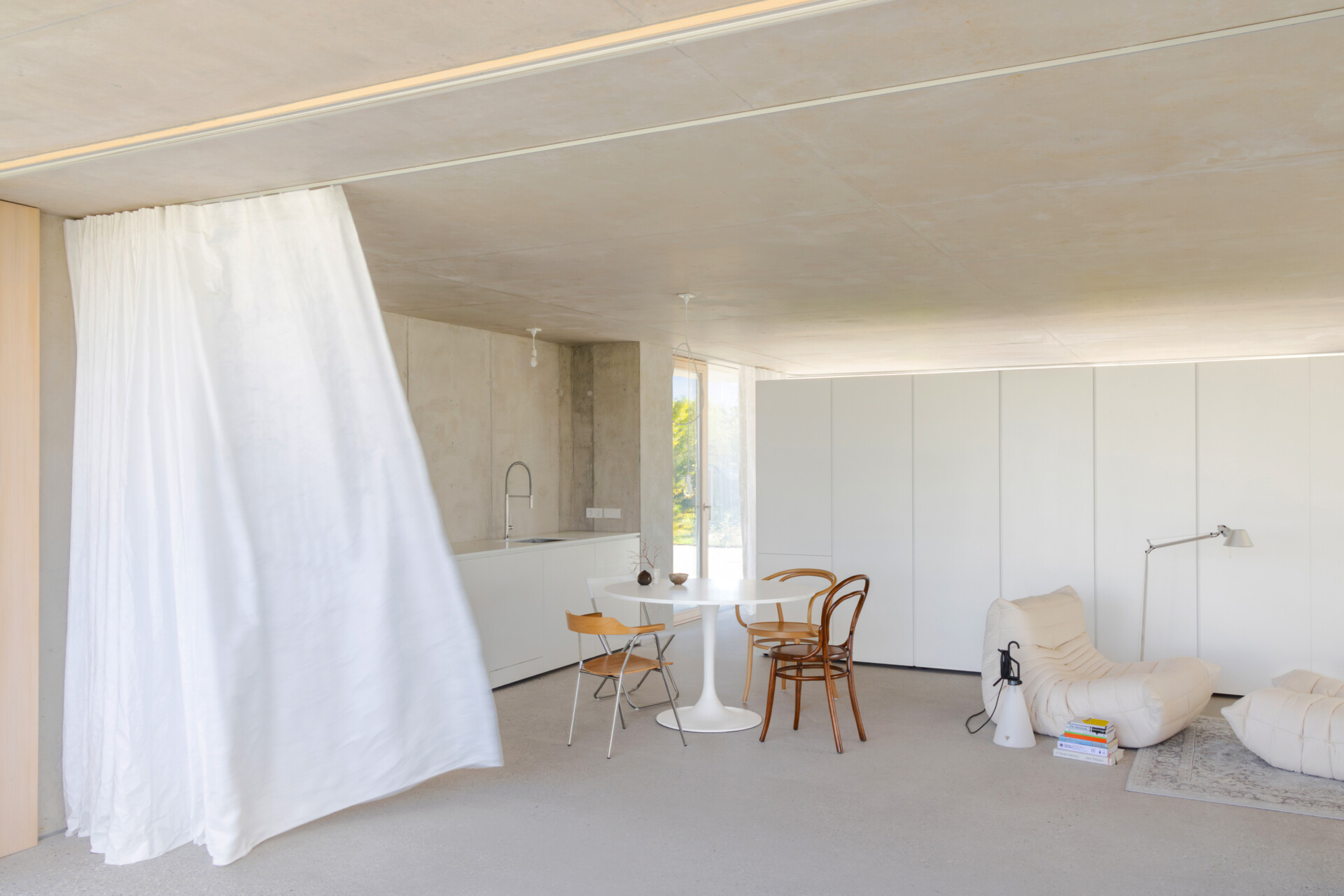 An open plan living, dining and kitchen layout with polished concrete floors, a cast iron fireplace, and a double sided storage wall separating the bedroom and living zones.