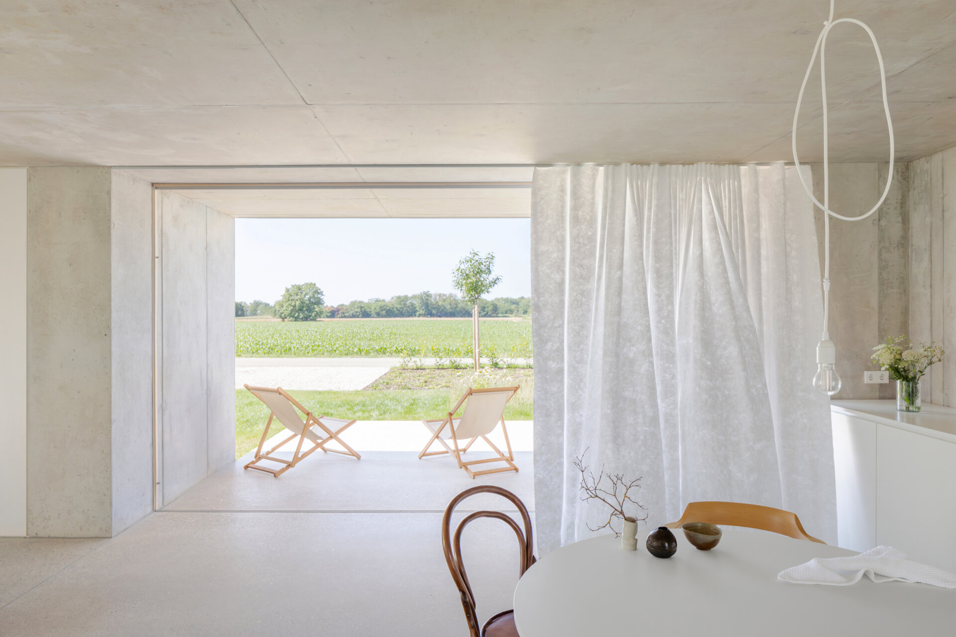 An open plan living, dining and kitchen layout with polished concrete floors, a cast iron fireplace, and a double sided storage wall separating the bedroom and living zones.
