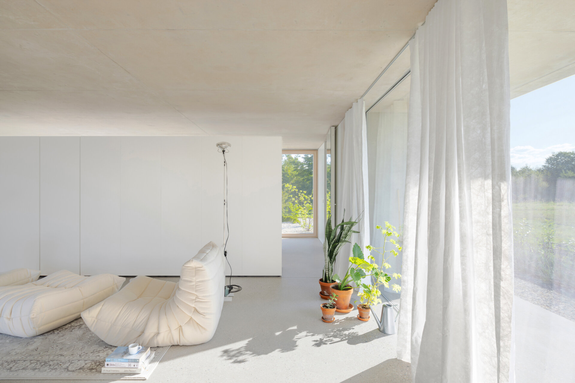An open plan living, dining and kitchen layout with polished concrete floors, a cast iron fireplace, and a double sided storage wall separating the bedroom and living zones.
