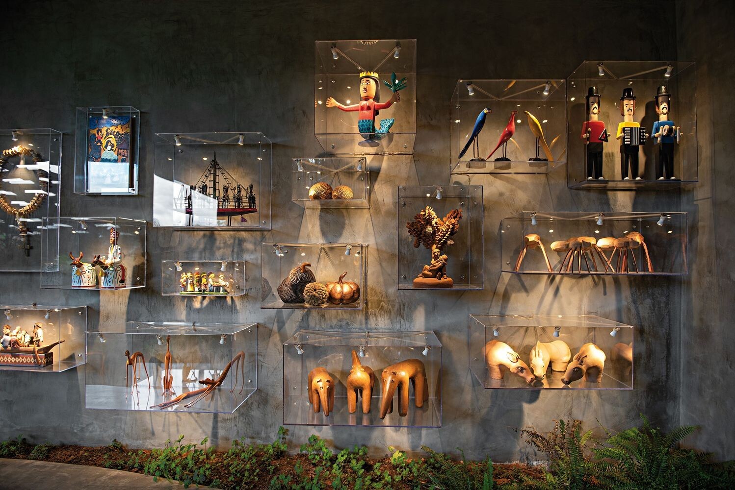 Arrival at the home is marked by a sequence of strong visual elements. An oversized black-framed glass door sets the tone, paired with stairs finished with black railings.

Along the way, a wall with clear floating boxes display sculptural pieces, while surrounding gardens soften the experience. Together, these details create a layered and striking entrance that blends architecture with curated moments.