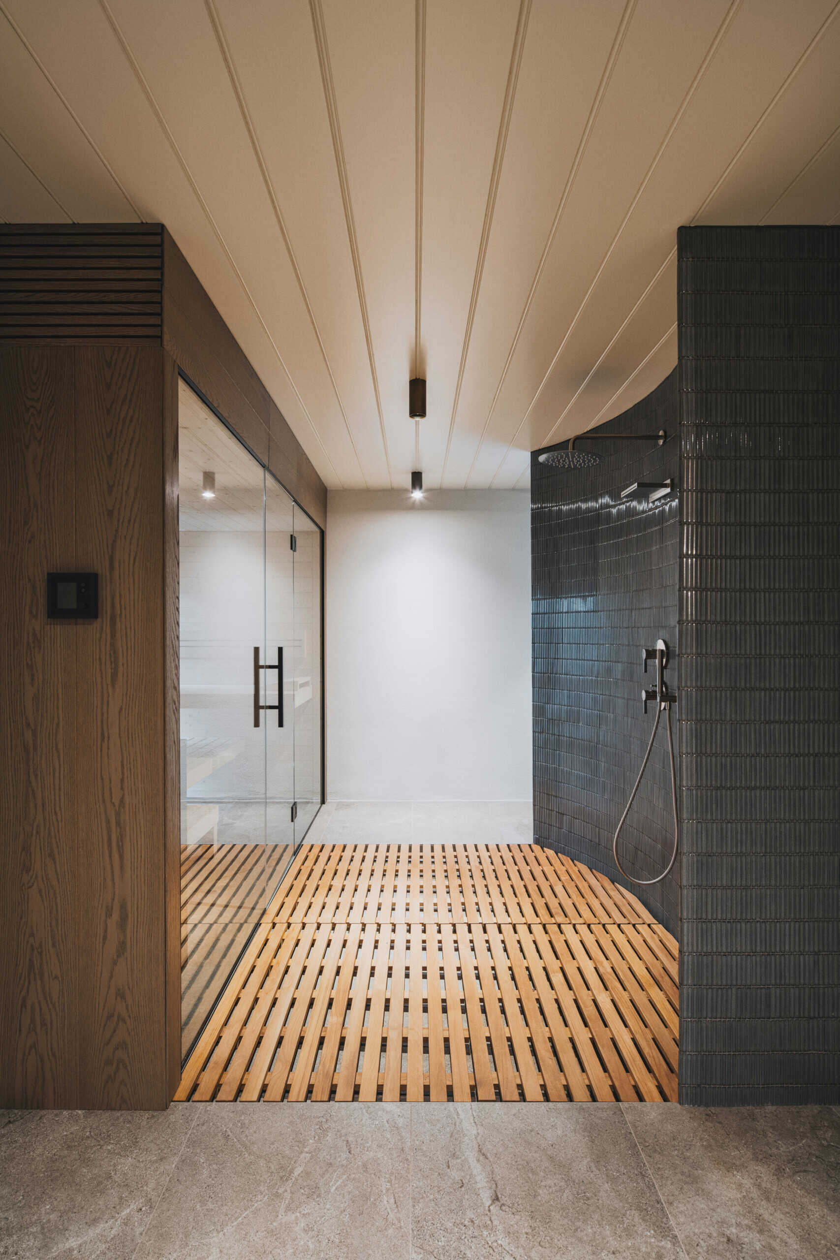 Clean lines and warm wood turn define this sauna zone. A glass wall reveals the pale, steamy interior, while the slatted wood mat underfoot adds softness. To the right, glossy tile wraps a gentle curve around the shower, paired with a simple hand sprayer. The light ceiling panels and small downlights keep everything bright and calm.