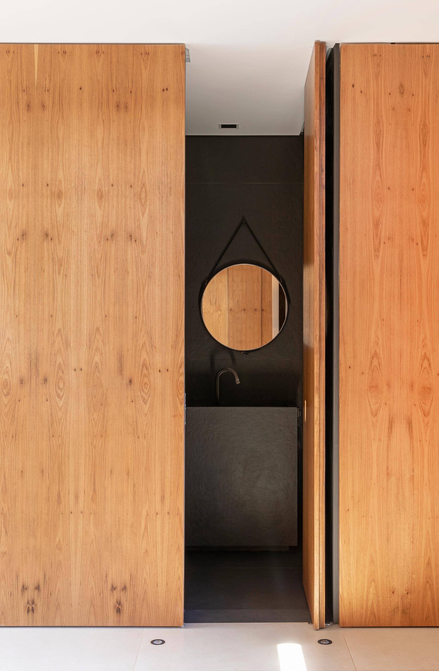 A dark-colored bathroom tucked behind a wood wall offers subtle luxury and visual integration.