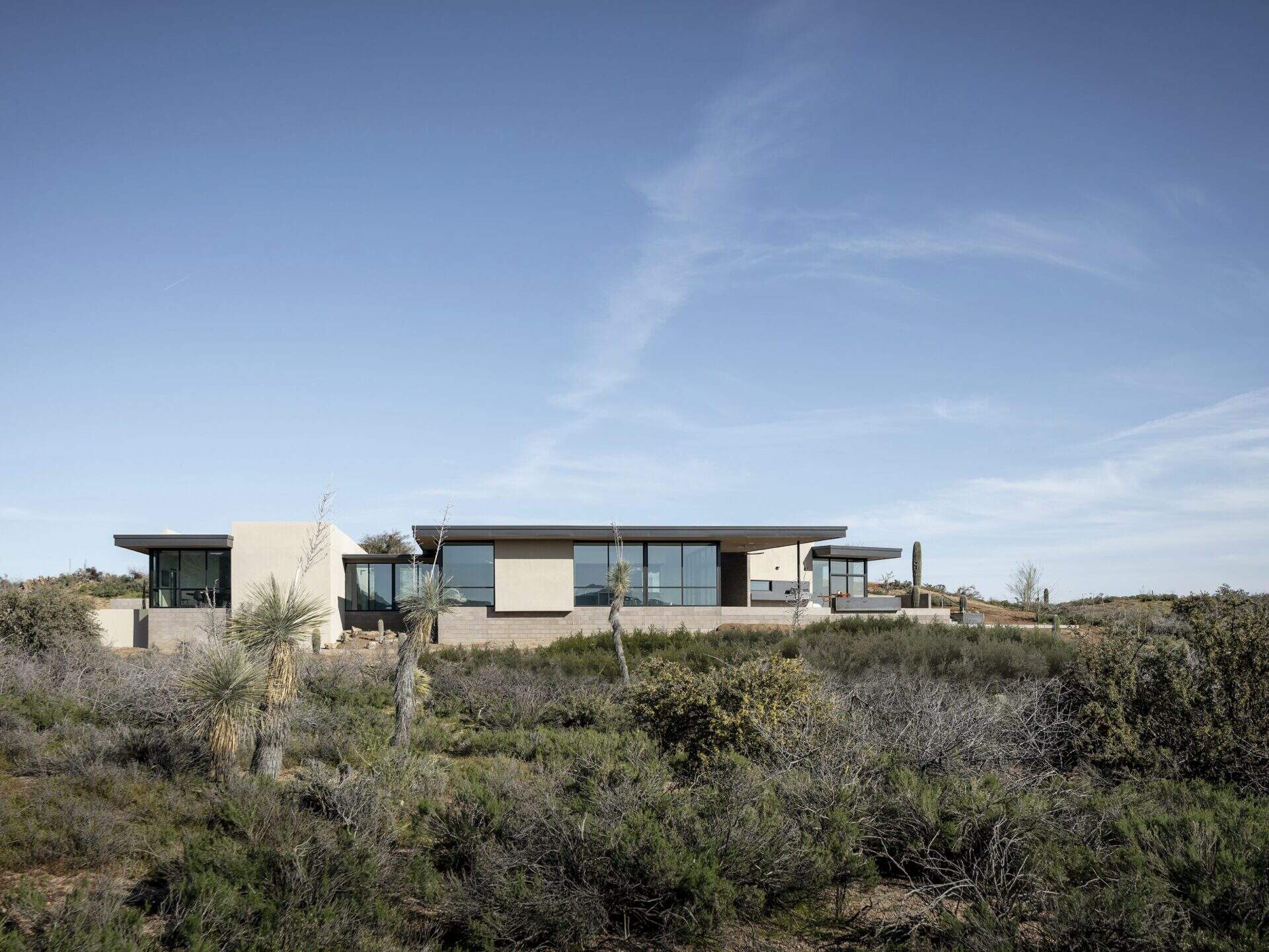 A modern desert home with exposed concrete block, glass, and deep roof overhangs designed for shade.