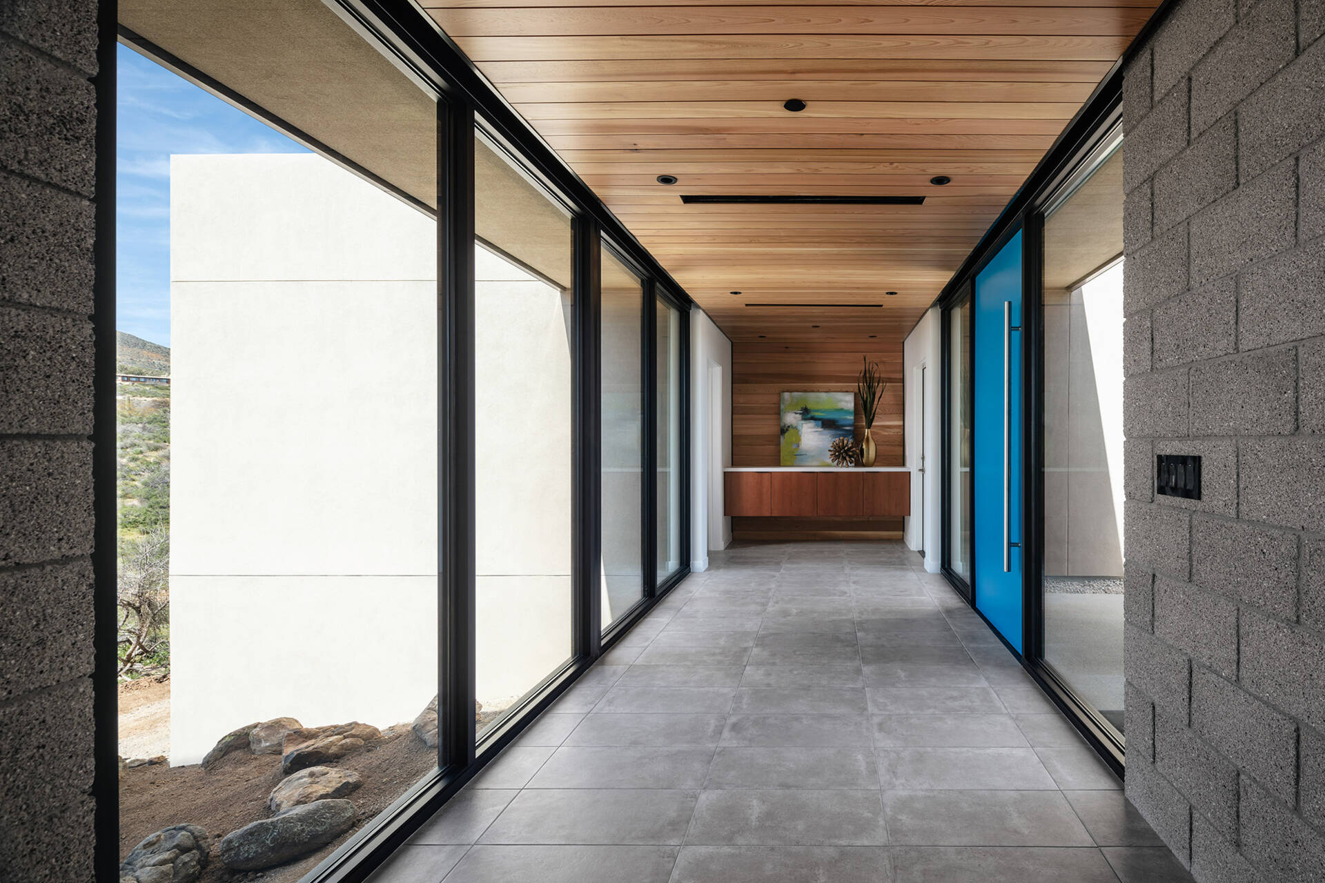 A glass bridge entry with a bold blue door and a floating wood ceiling that extends into a feature wall.