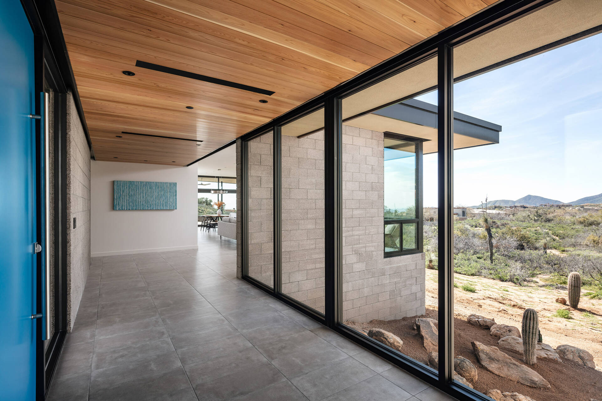 A glass bridge entry with a bold blue door and a floating wood ceiling that extends into a feature wall.