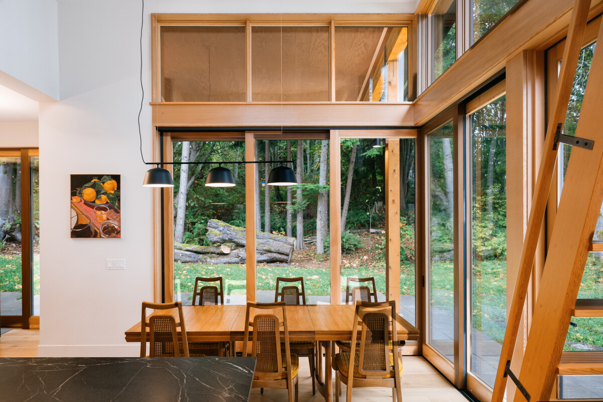 A double-height glass corner dining space that captures sweeping views of trees, water, and sky.