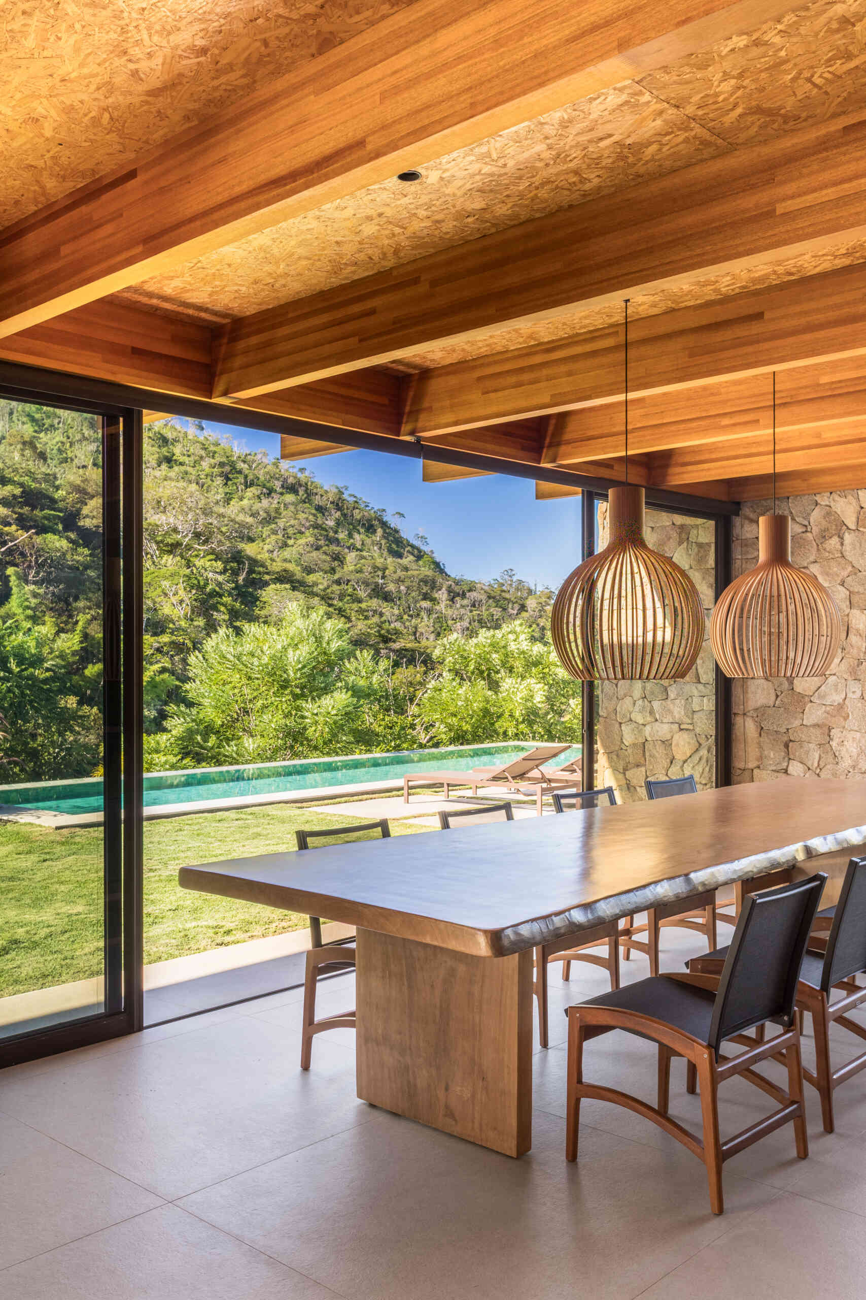 The dining area continues with the natural warmth, with a live-edge table positioned beneath woven pendant lights, while sliding glass doors open to the outdoors.