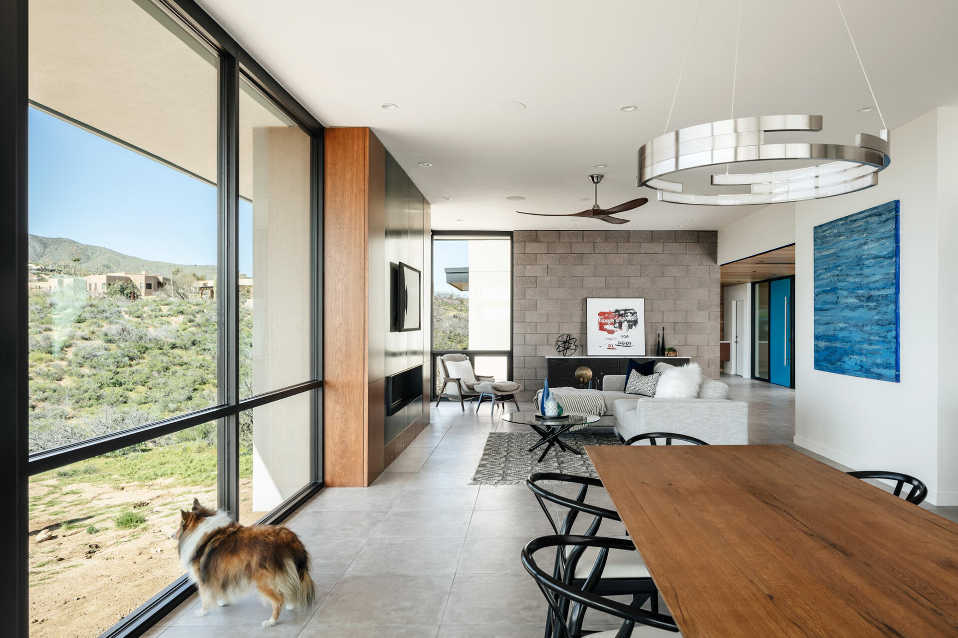A living and dining space with warm wood cabinetry, steel accents, and full-height glass opening to the patio.