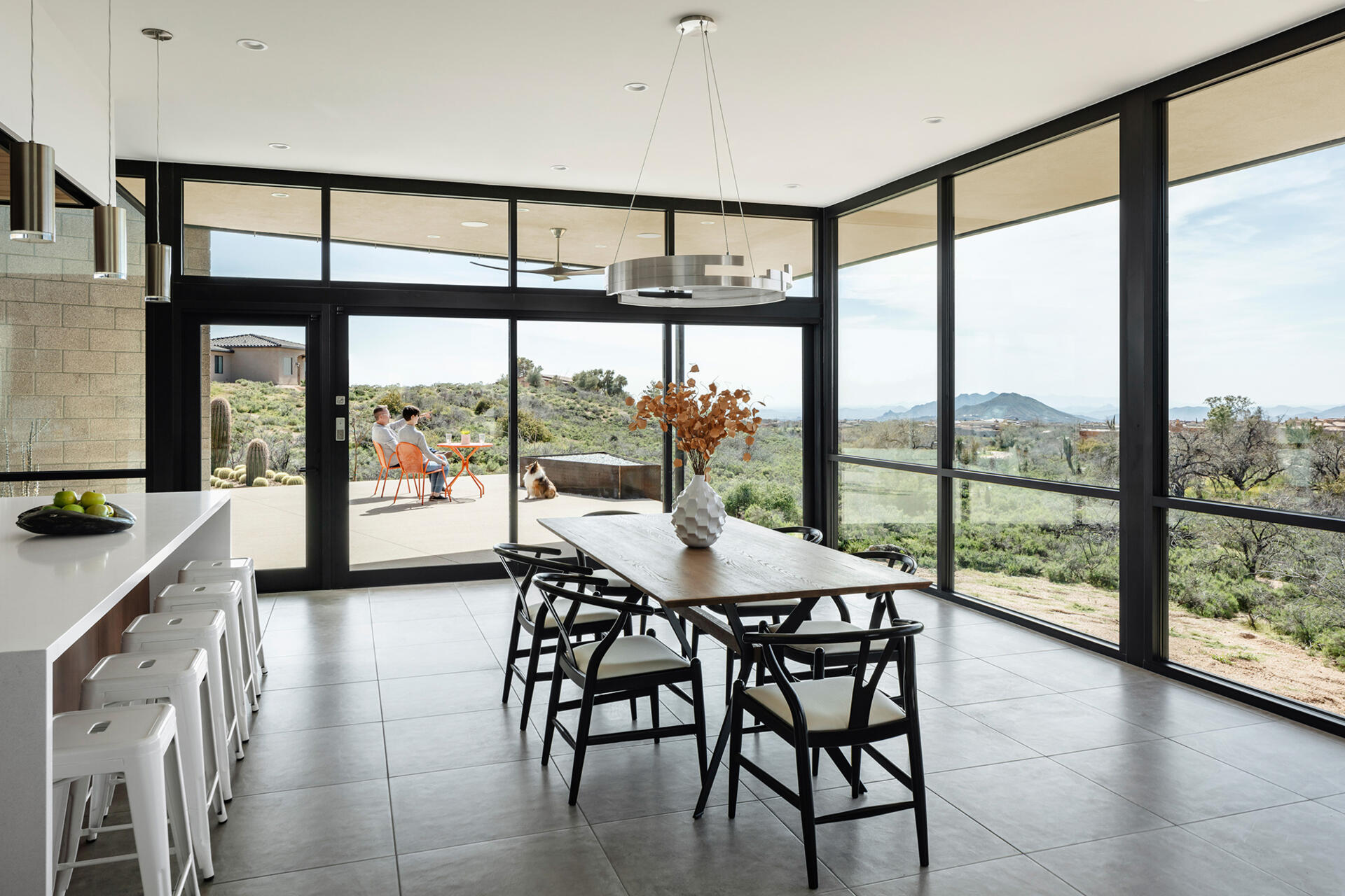 A living and dining space with warm wood cabinetry, steel accents, and full-height glass opening to the patio.
