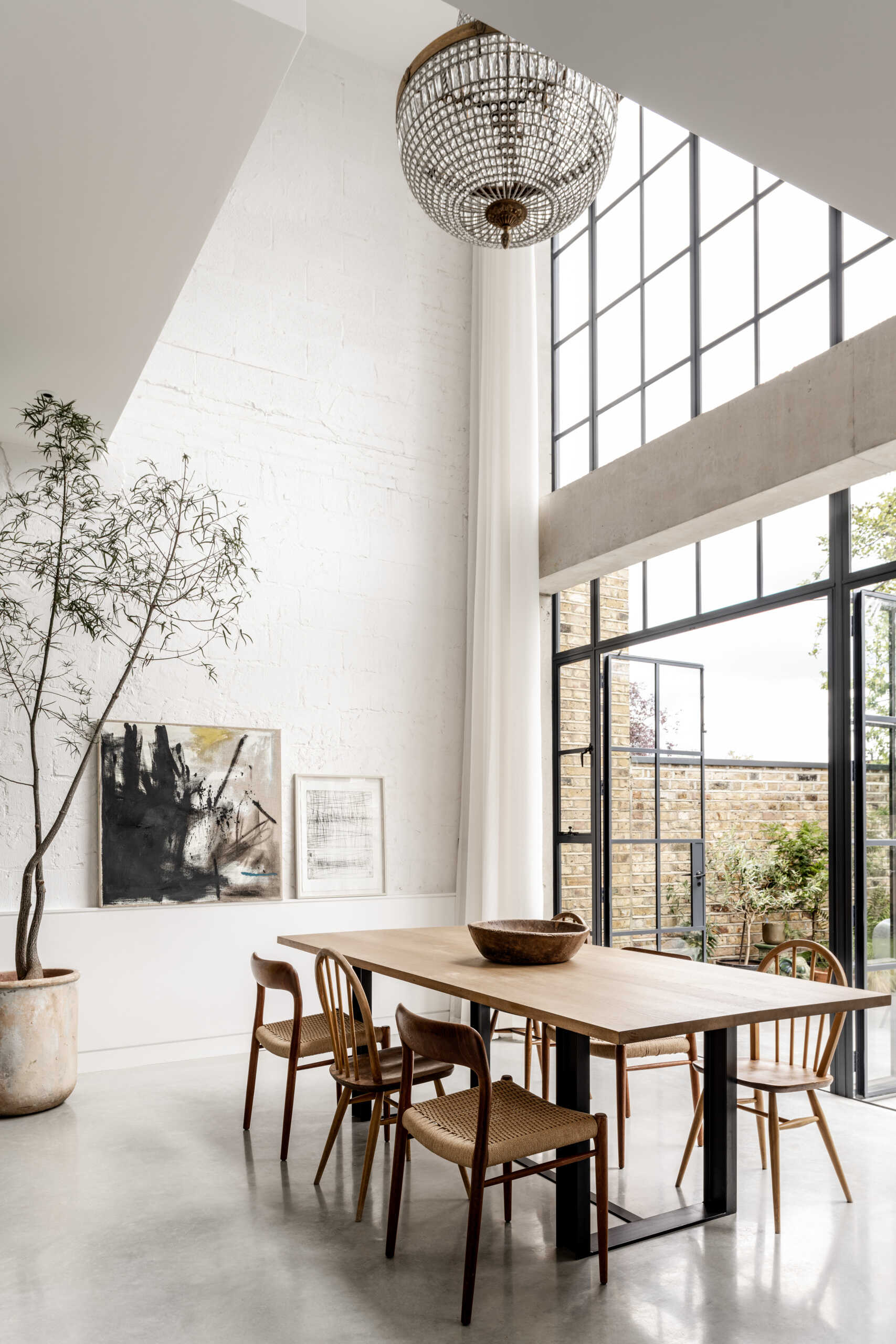 In the dining room, floor-to-ceiling glazing fills the space with natural light while framing views of the garden and the willow tree that anchors the outdoor space.