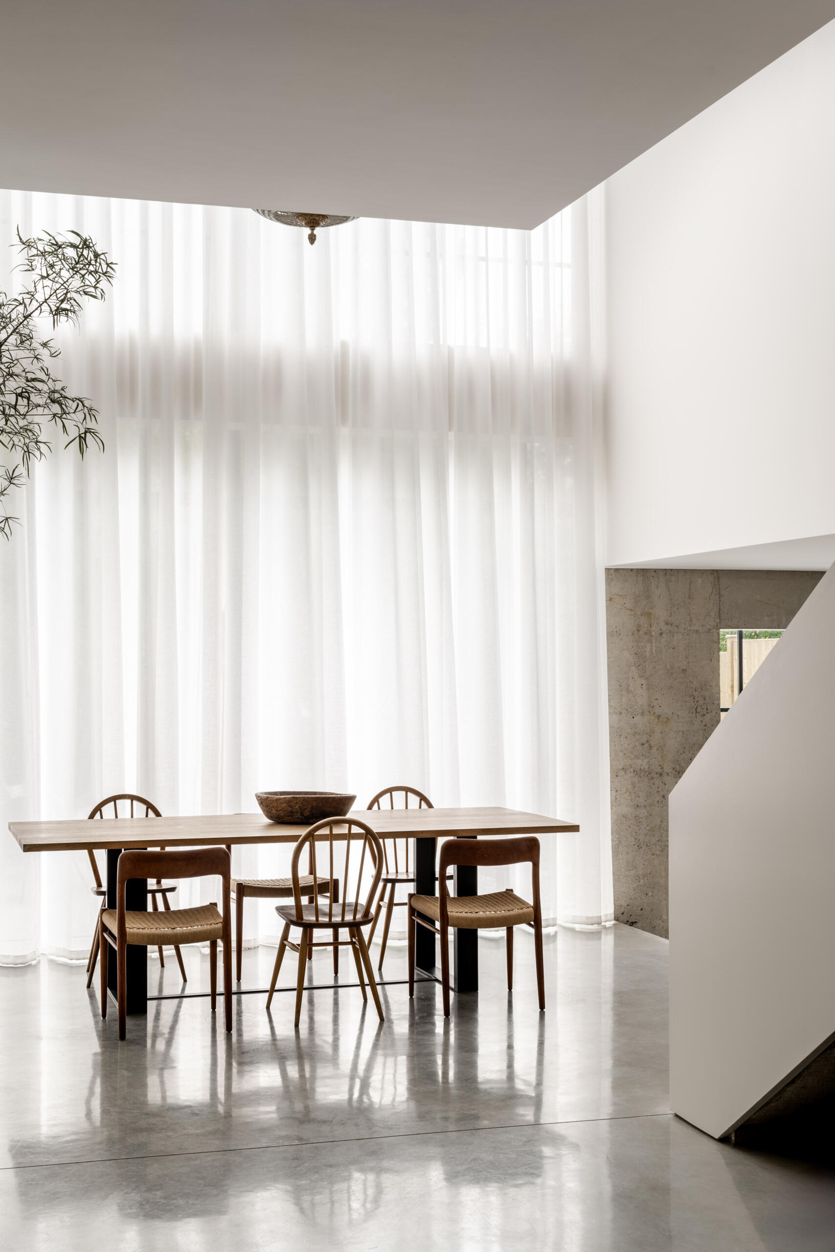 In the dining room, floor-to-ceiling glazing fills the space with natural light while framing views of the garden and the willow tree that anchors the outdoor space.