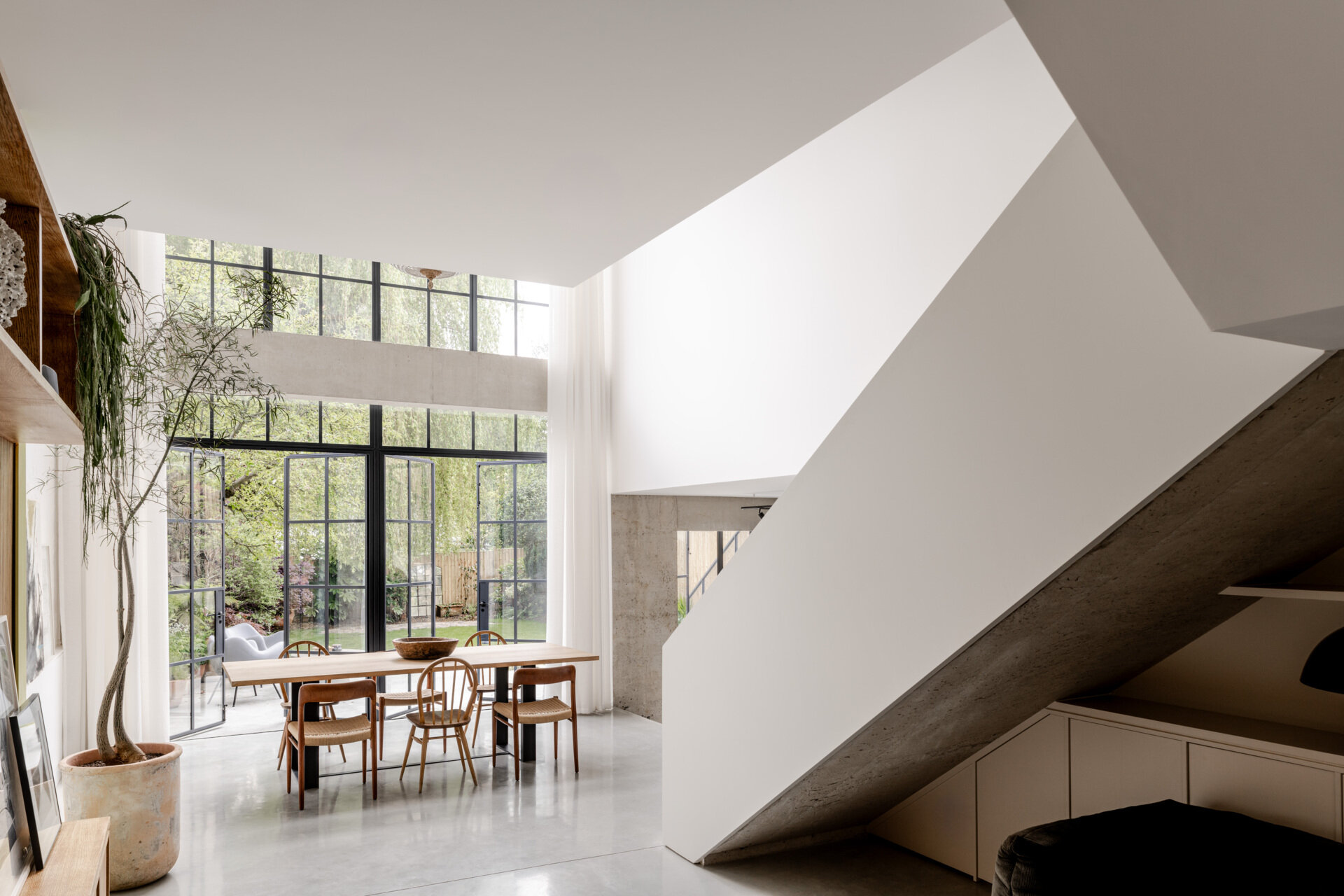 In the dining room, floor-to-ceiling glazing fills the space with natural light while framing views of the garden and the willow tree that anchors the outdoor space.