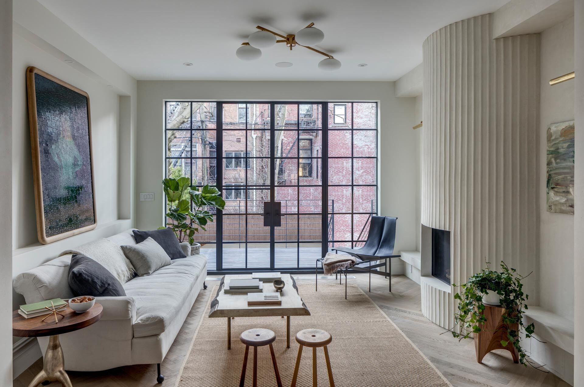 A floor to ceiling fluted plaster fireplace transforms this 1860s Brooklyn living room into a sculptural focal point, balanced by steel doors, built in shelving, and curated art.