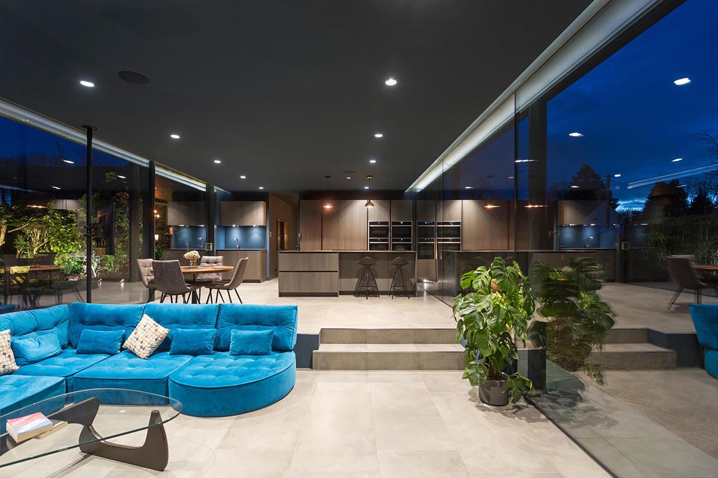 At night, the glass extension glows softly, with the garden becoming a striking backdrop through the glass walls.