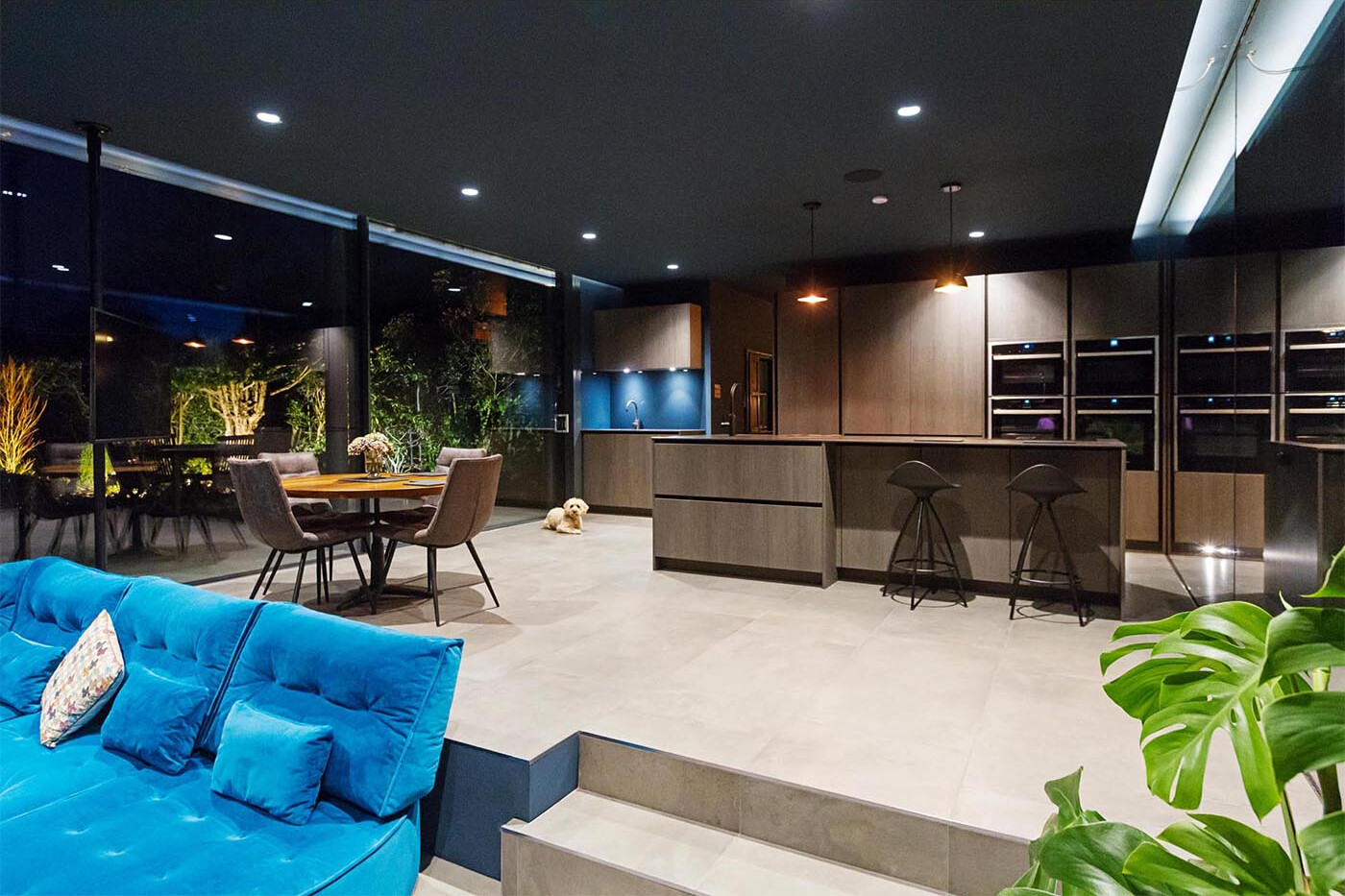 At night, the glass extension glows softly, with the garden becoming a striking backdrop through the glass walls.